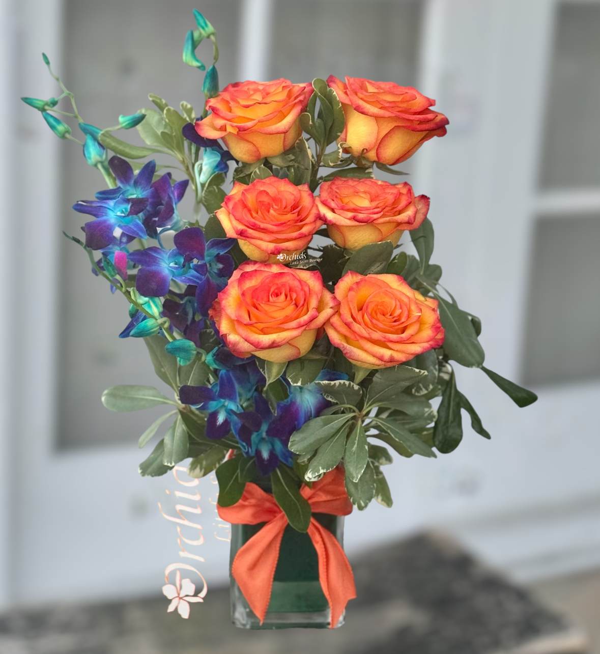 Orange roses with blue orchids in a glass vase