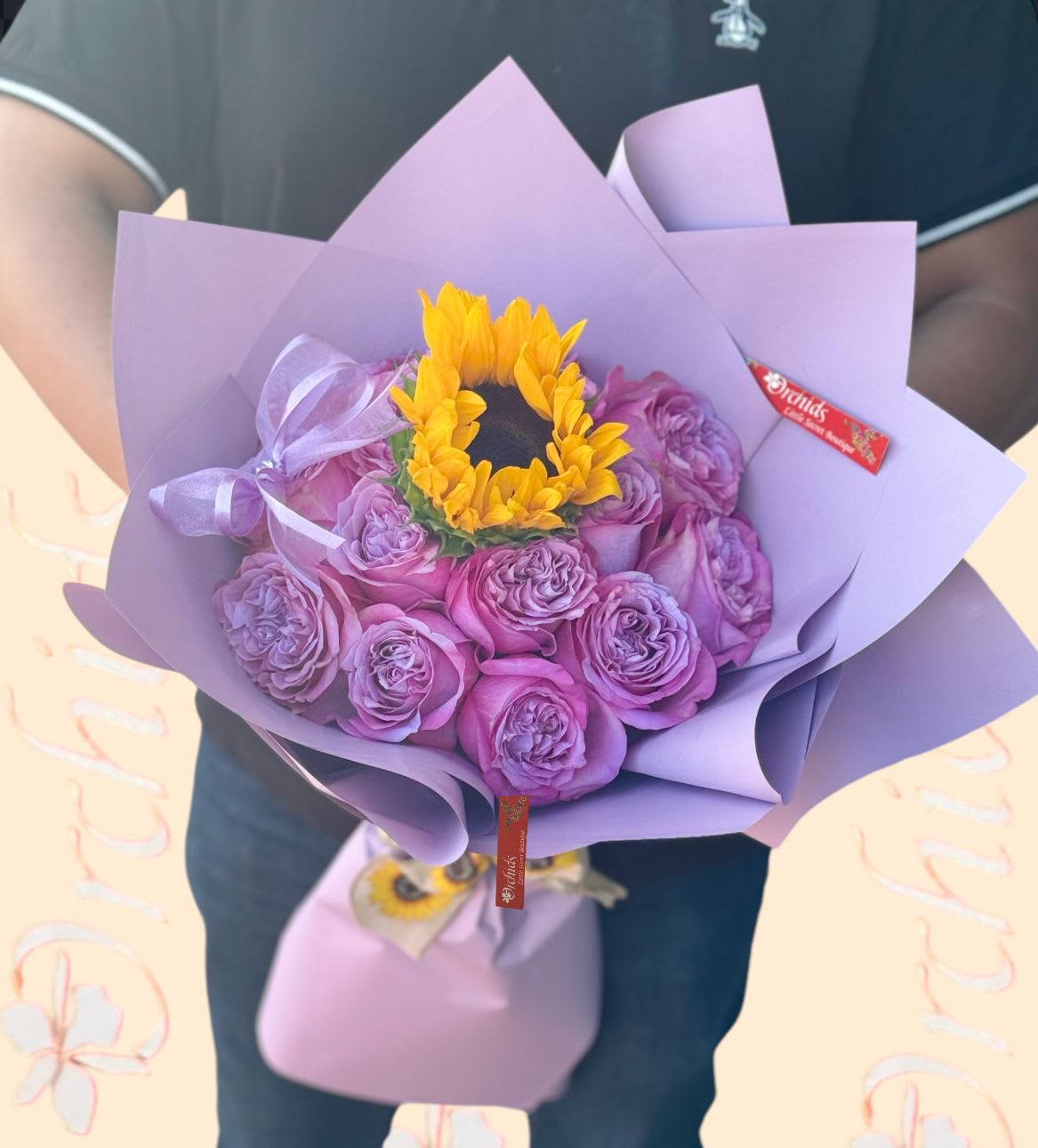Bouquet of purple roses with a yellow sunflower center wrapped in lavender paper