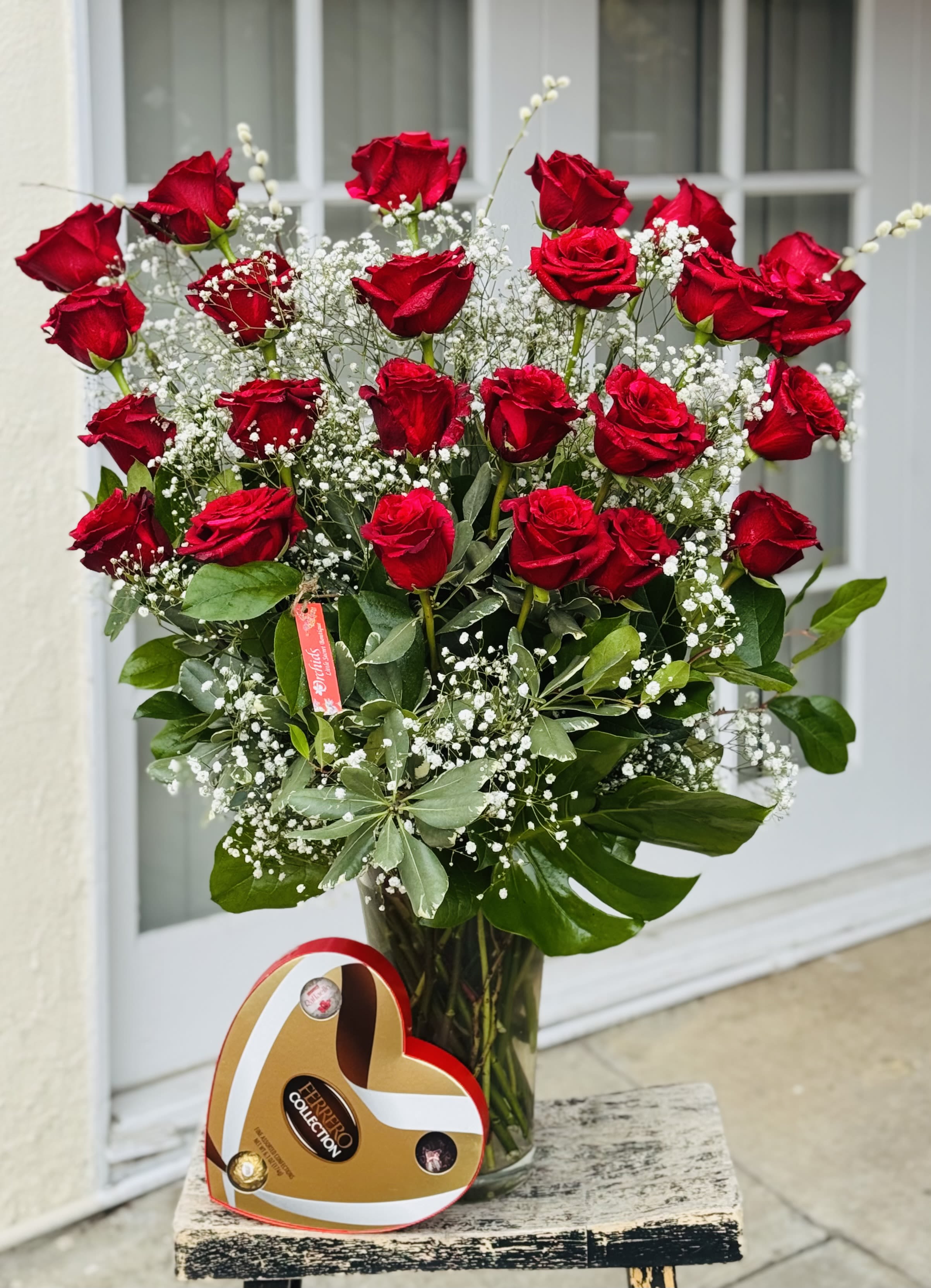 Bouquet of red roses in a glass vase with baby's breath and a heart-shaped chocolate box