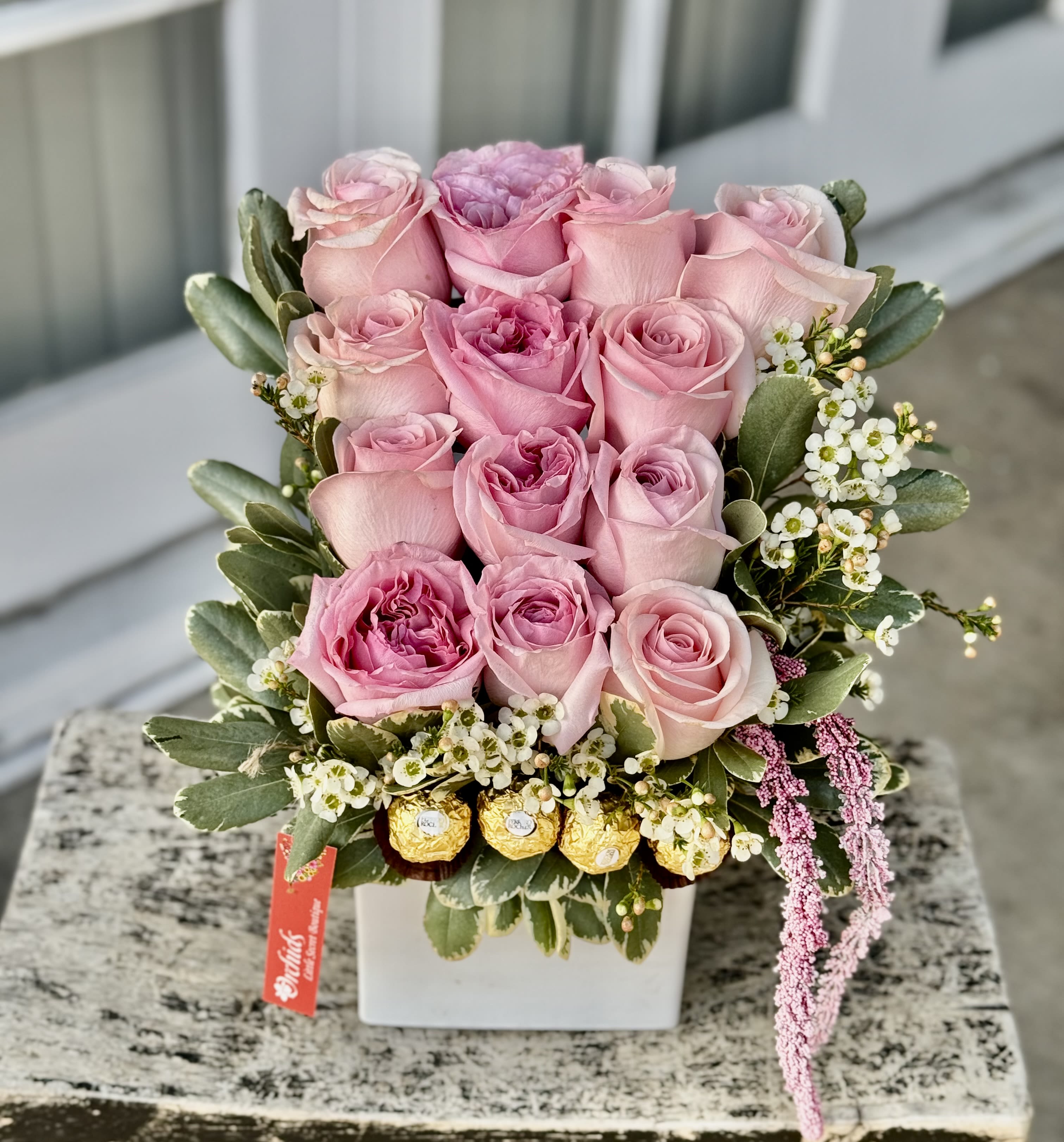 Pink roses arranged in a white square vase with small white filler flowers