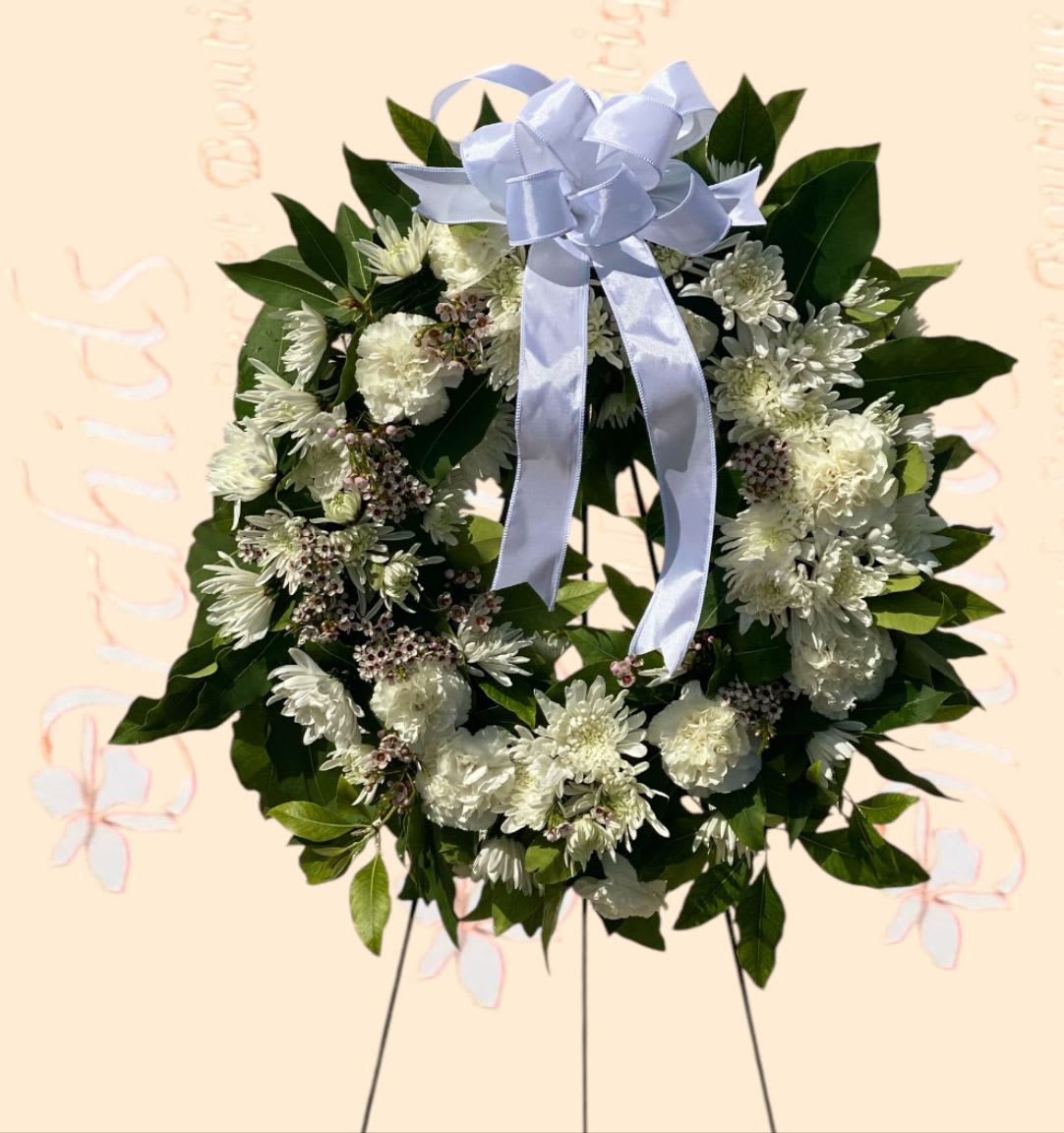White floral wreath with a pale blue ribbon bow on a stand