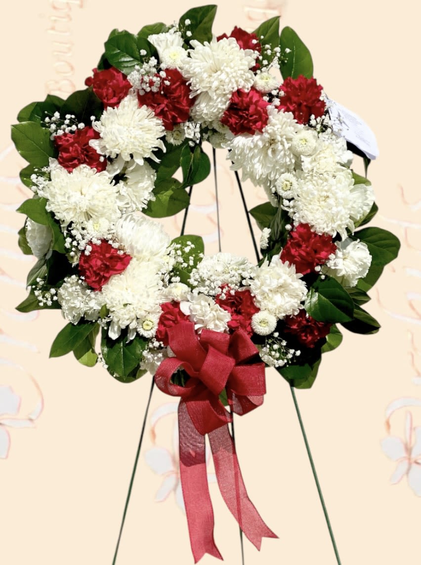 Red and white floral wreath with a red ribbon bow on a stand