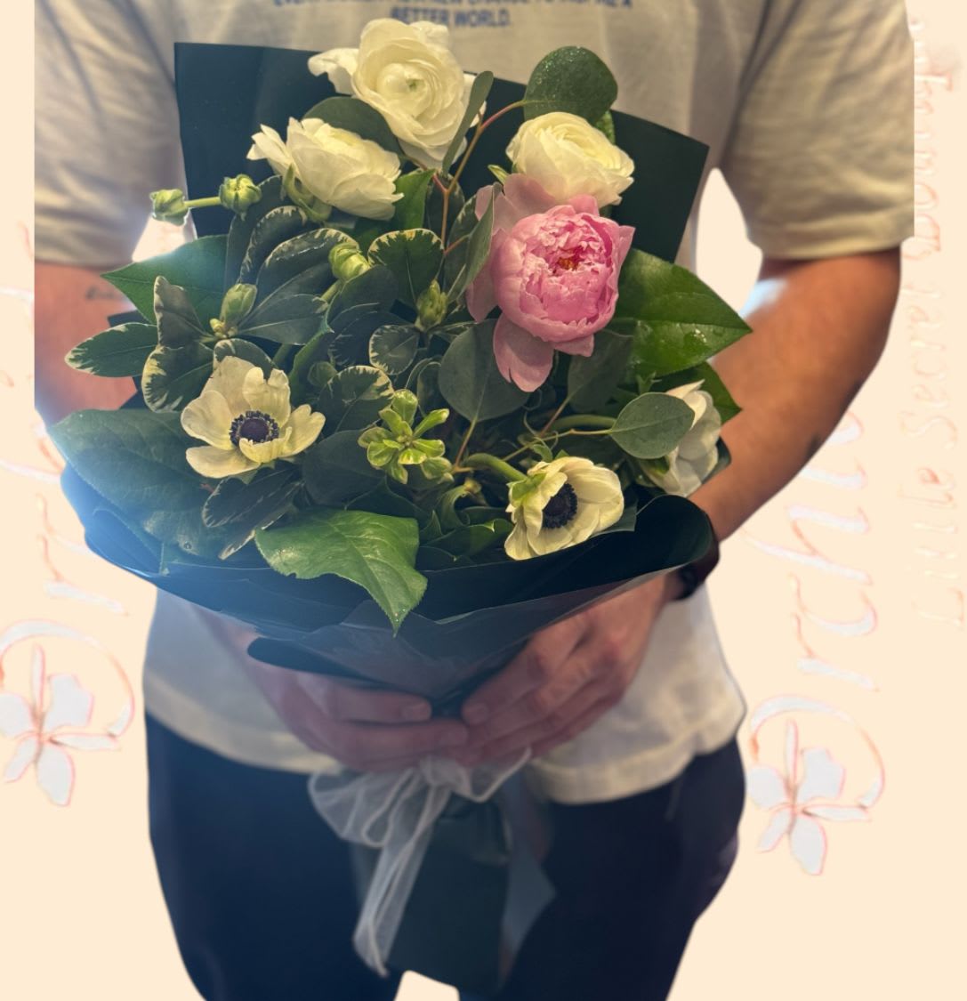 Handheld bouquet of white and pink flowers wrapped in dark paper