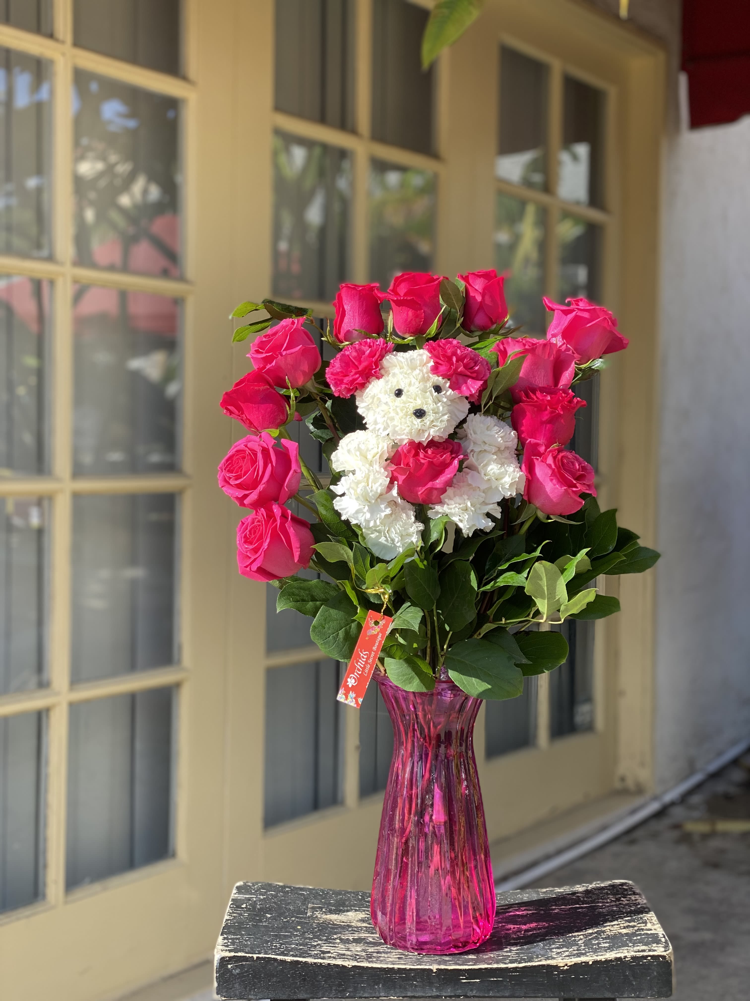 Pink roses arranged around a small white teddy bear in a pink vase