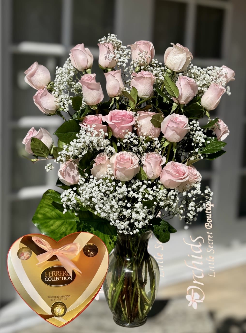 Pink roses in a glass vase with baby's breath and a heart-shaped chocolate box