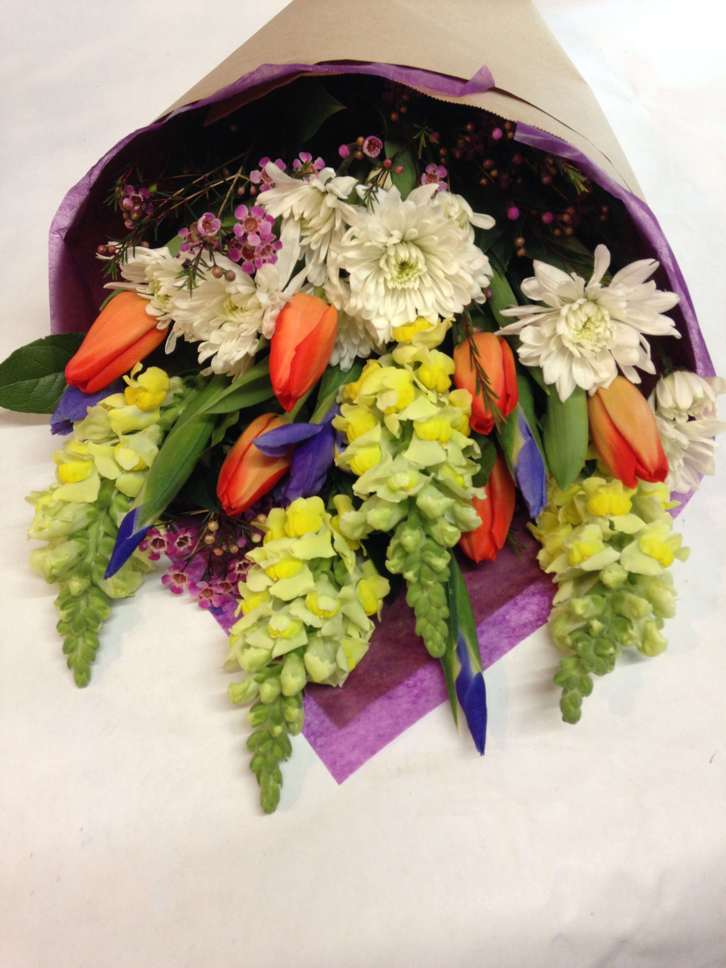 Bouquet of white daisies, orange tulips, and yellow snapdragons wrapped in purple paper