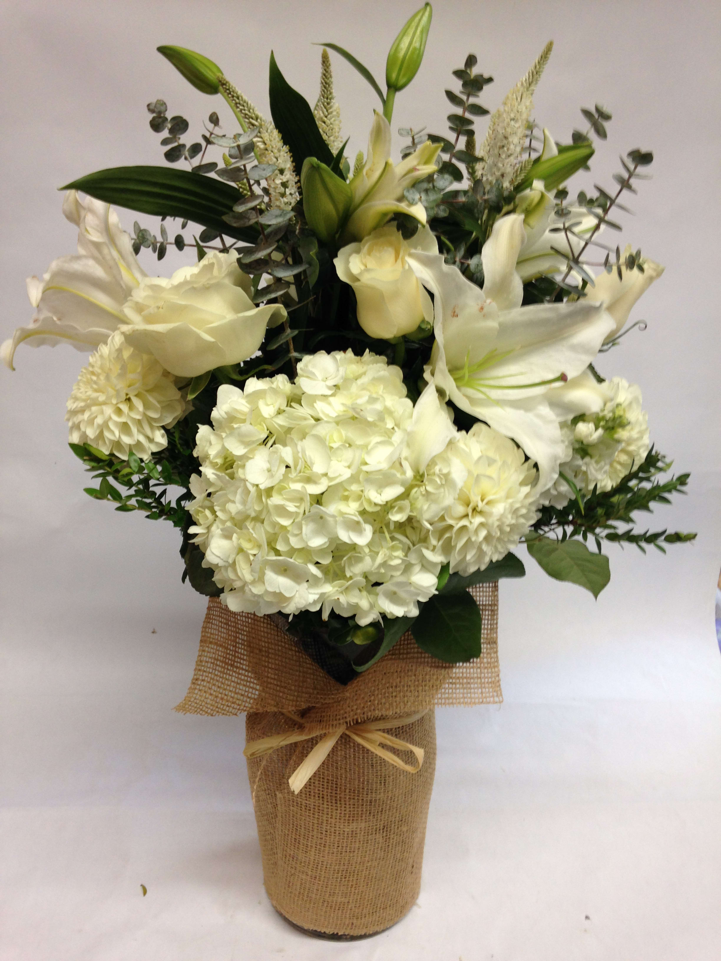 White lilies and hydrangeas arranged in a burlap-wrapped vase