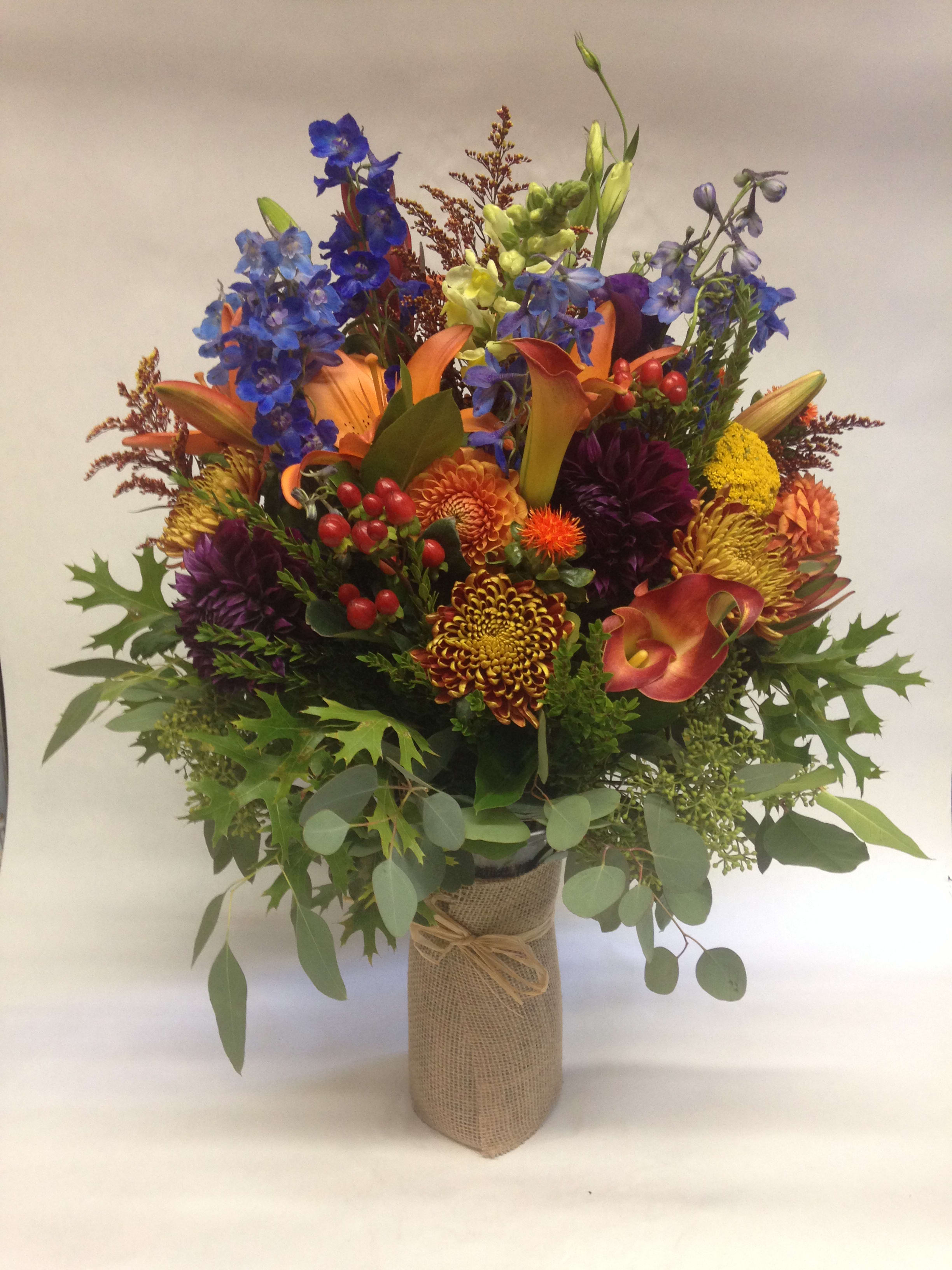 Colorful mixed bouquet with lilies, calla lilies, and chrysanthemums in a burlap-wrapped vase