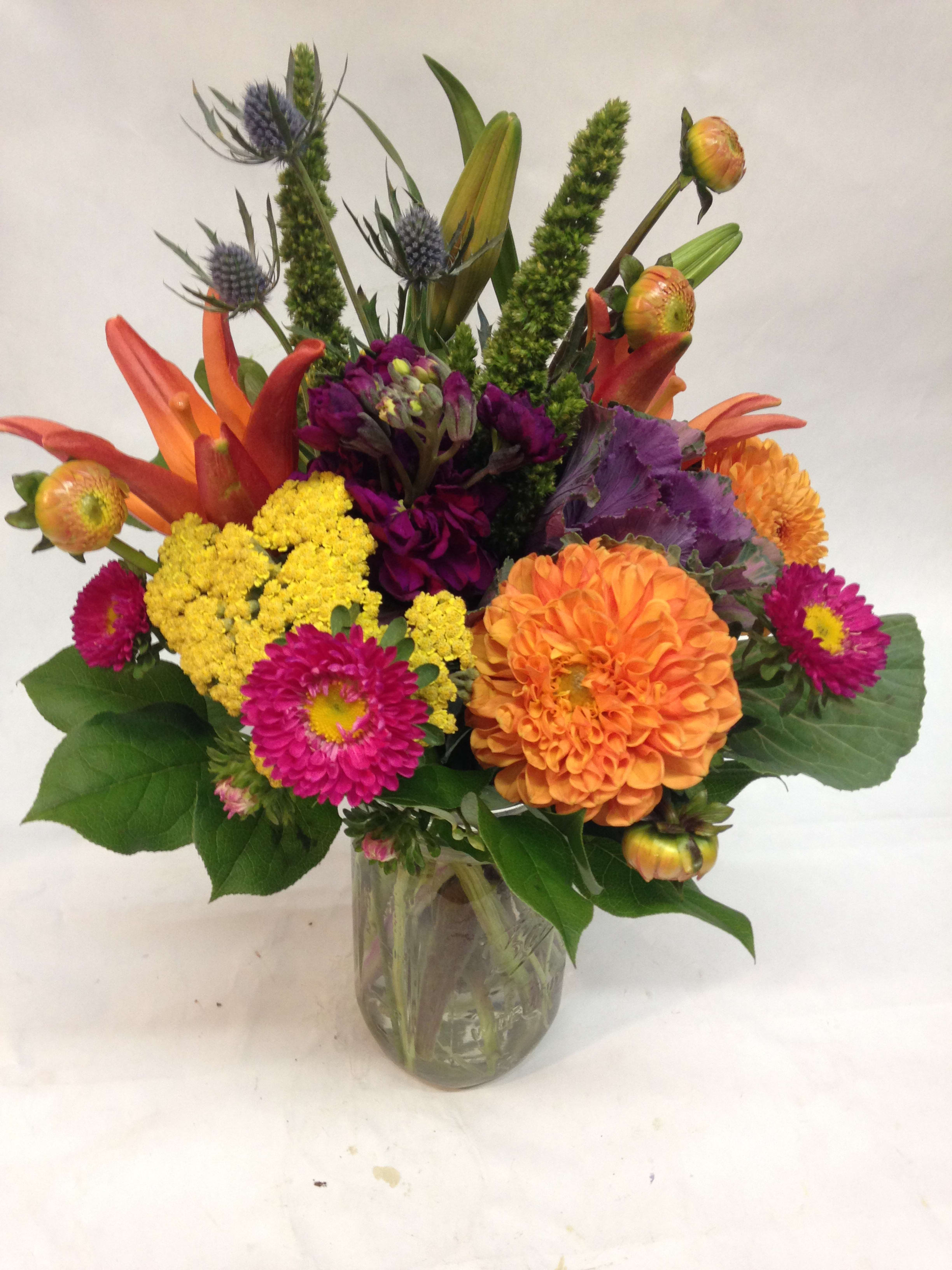 Bright mixed arrangement of orange, yellow, and pink flowers in a clear glass vase