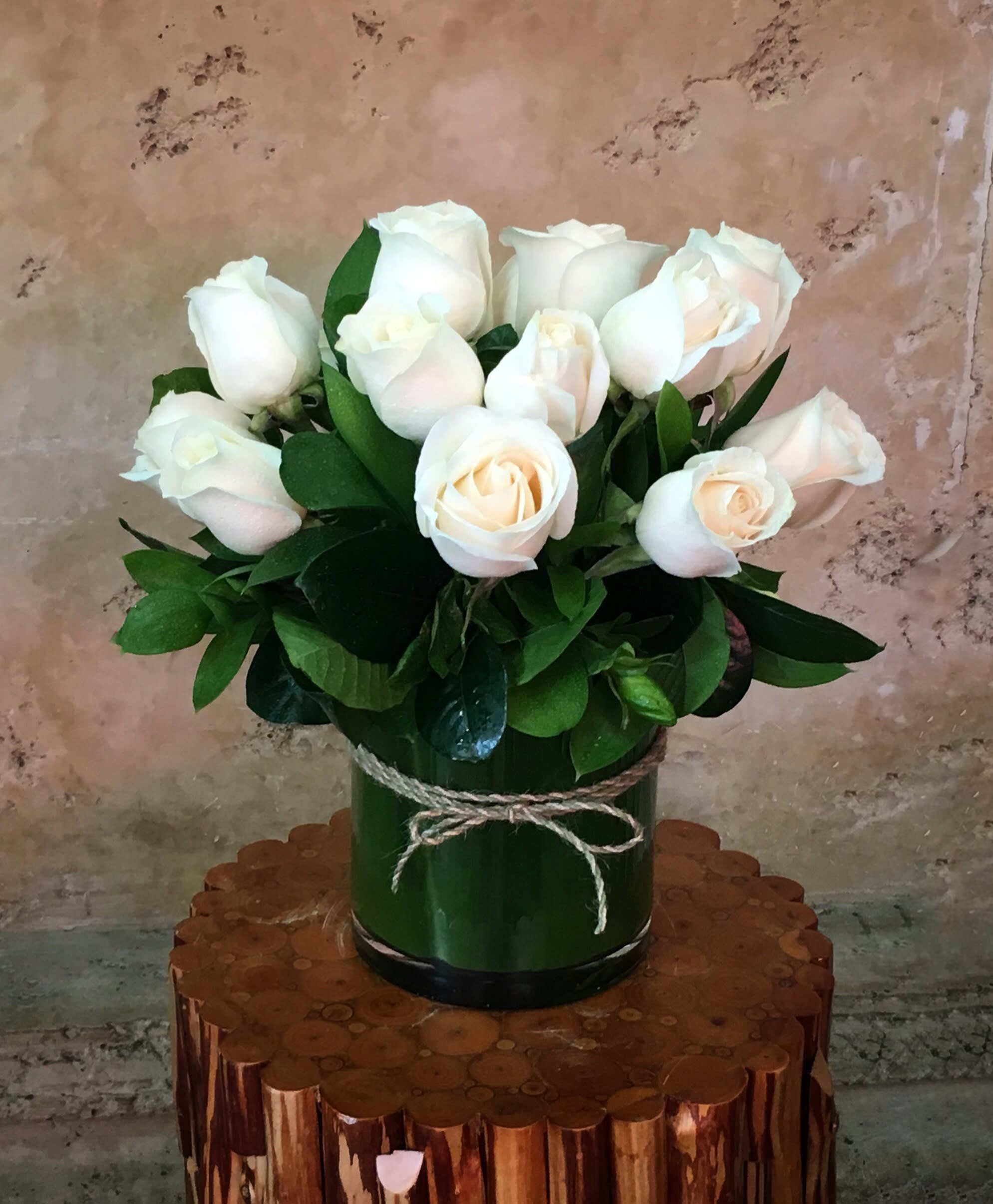 White roses in a green cylindrical vase tied with twine