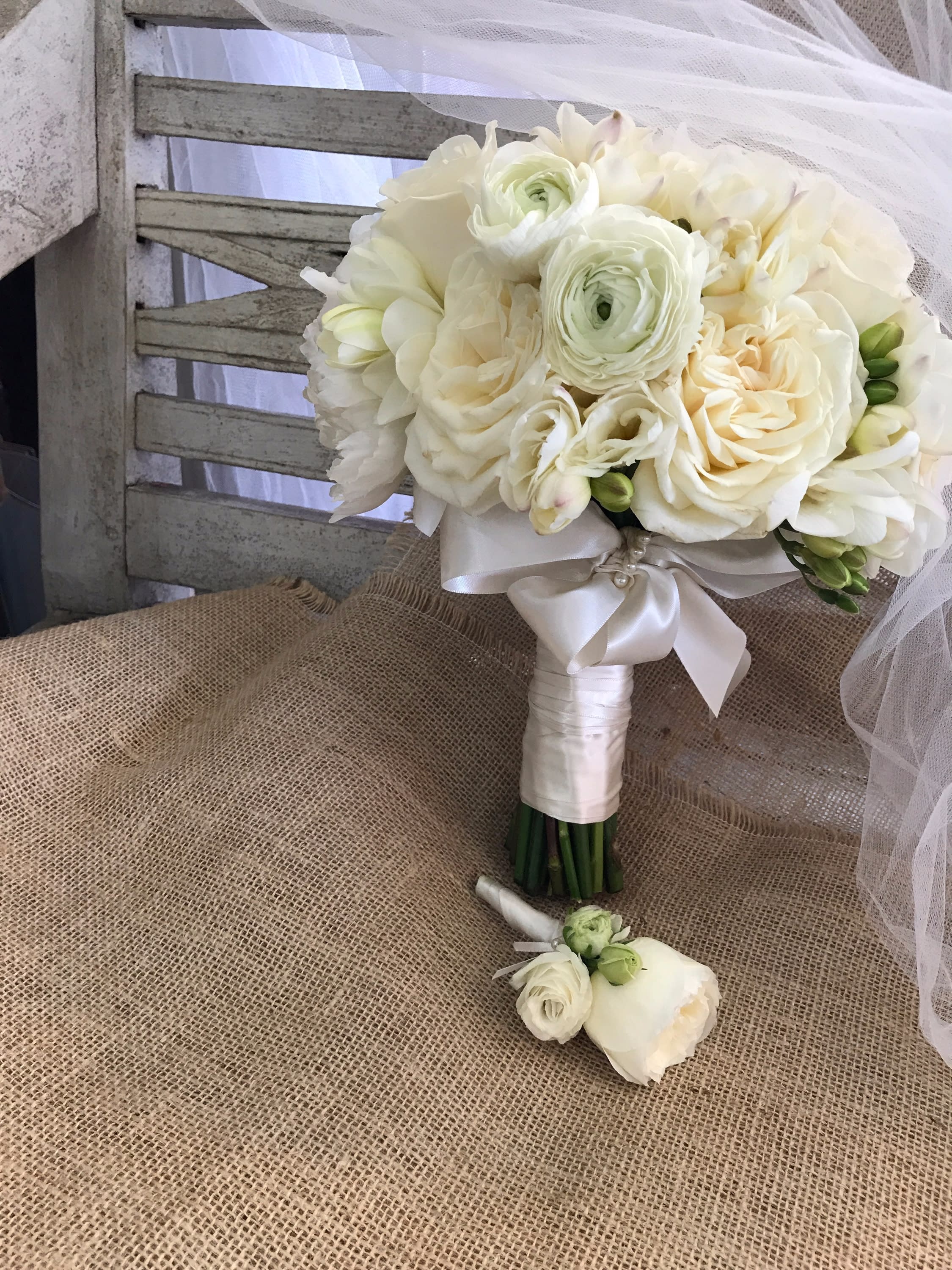 White bridal bouquet with roses and ranunculus, tied with satin ribbon