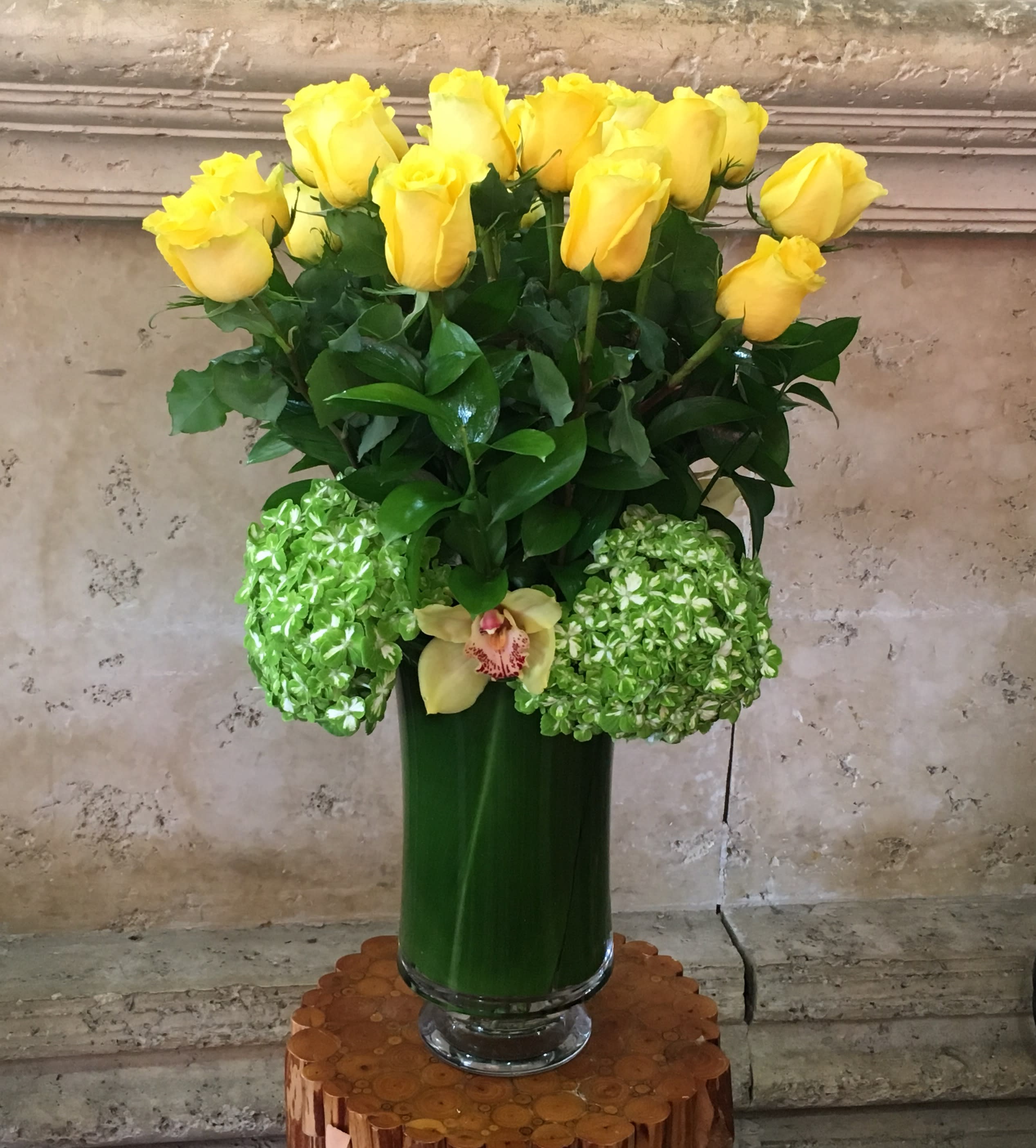 Yellow roses and green hydrangeas in a tall glass vase