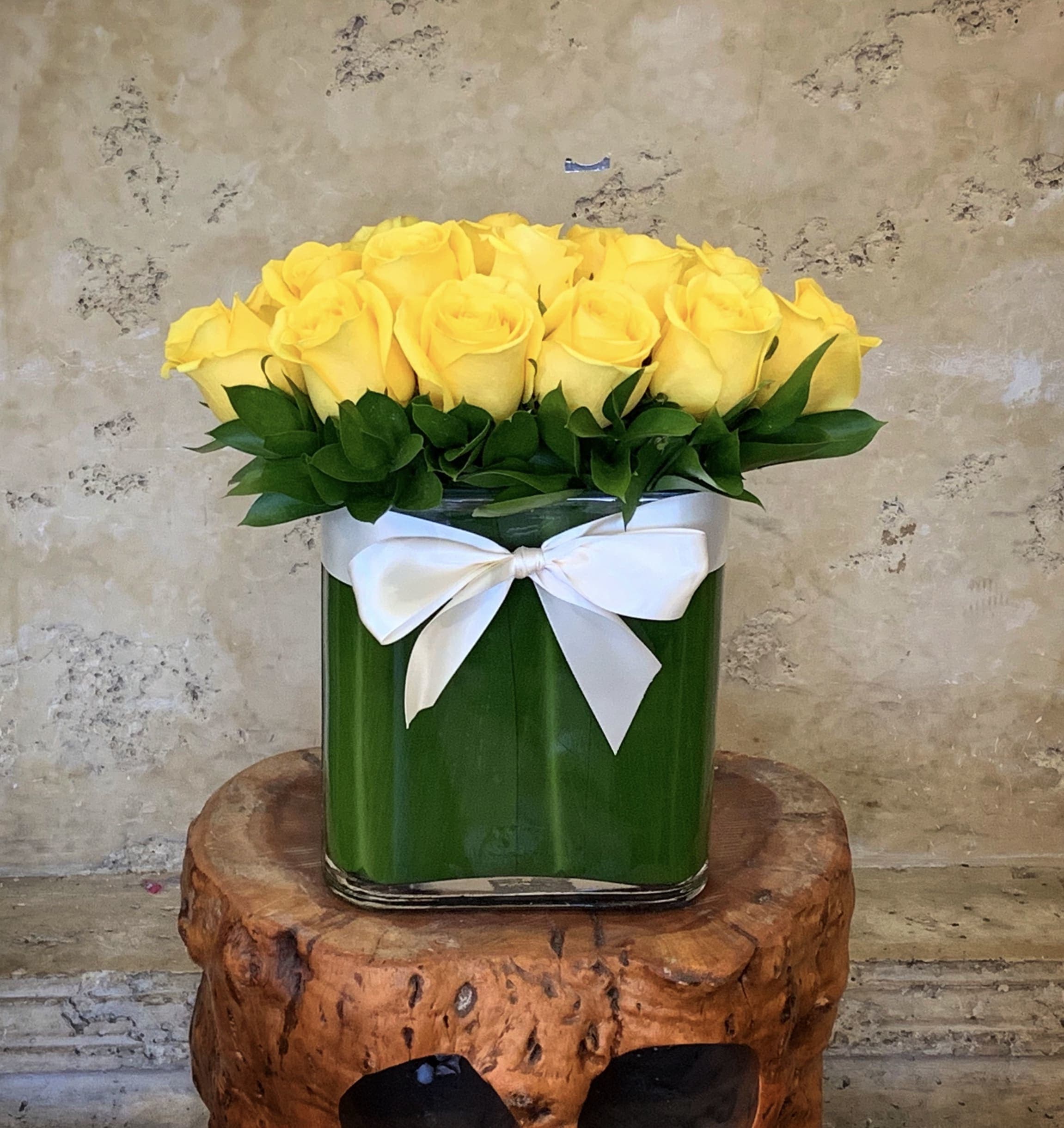 Yellow roses arranged in a square glass vase with a white ribbon