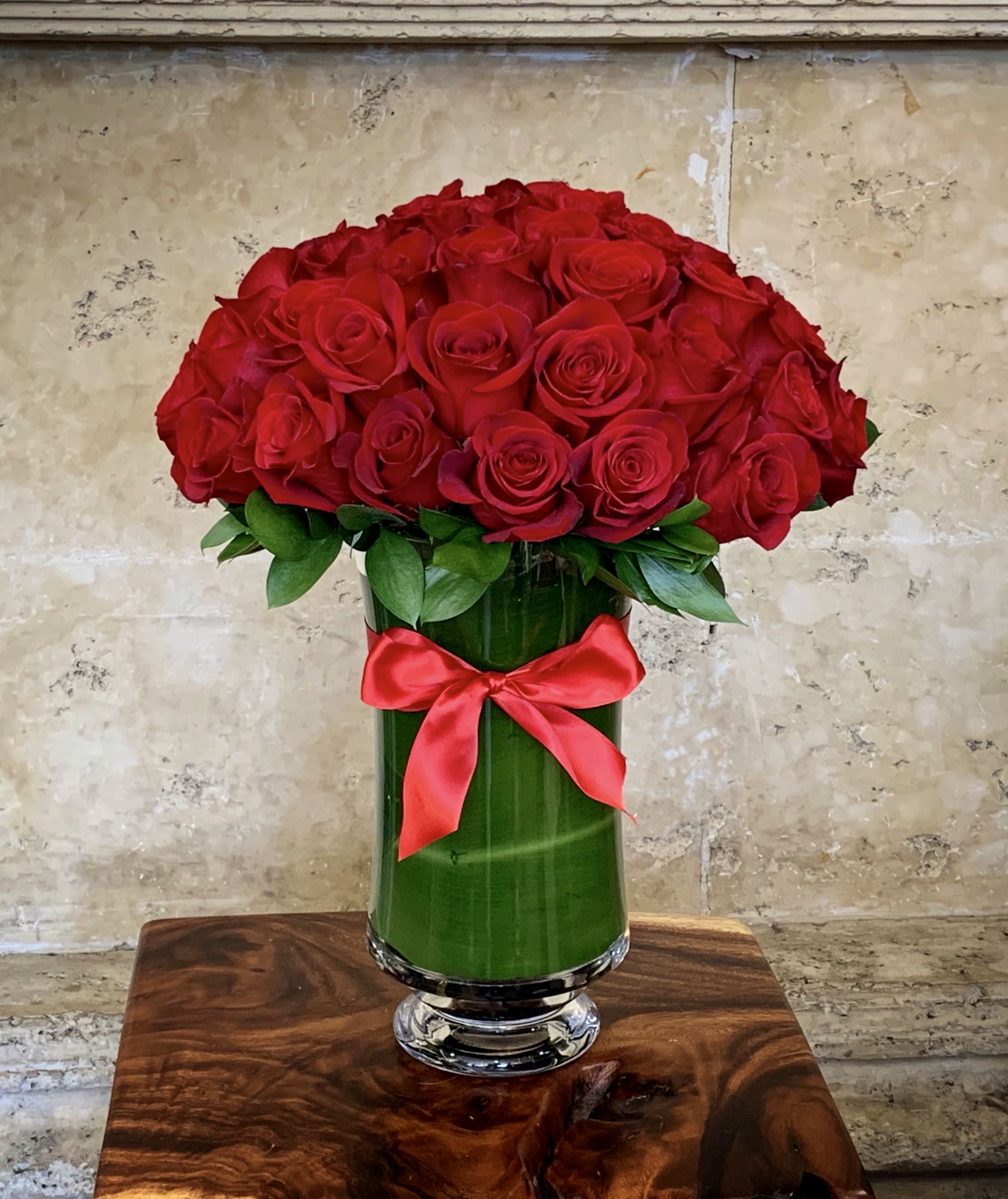 Red roses arranged in a tall glass vase with a red ribbon