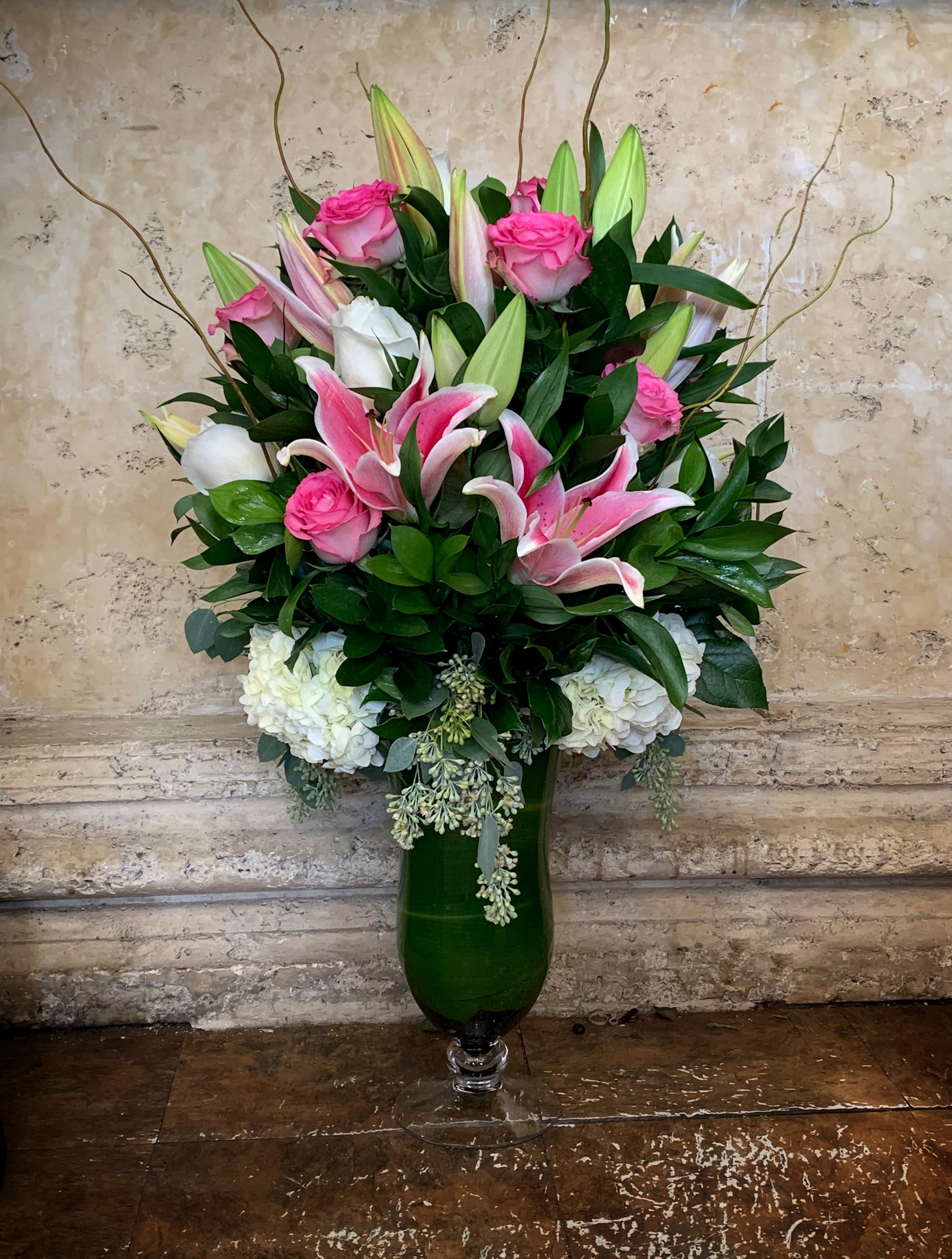 Pink roses and lilies arranged in a tall green glass vase