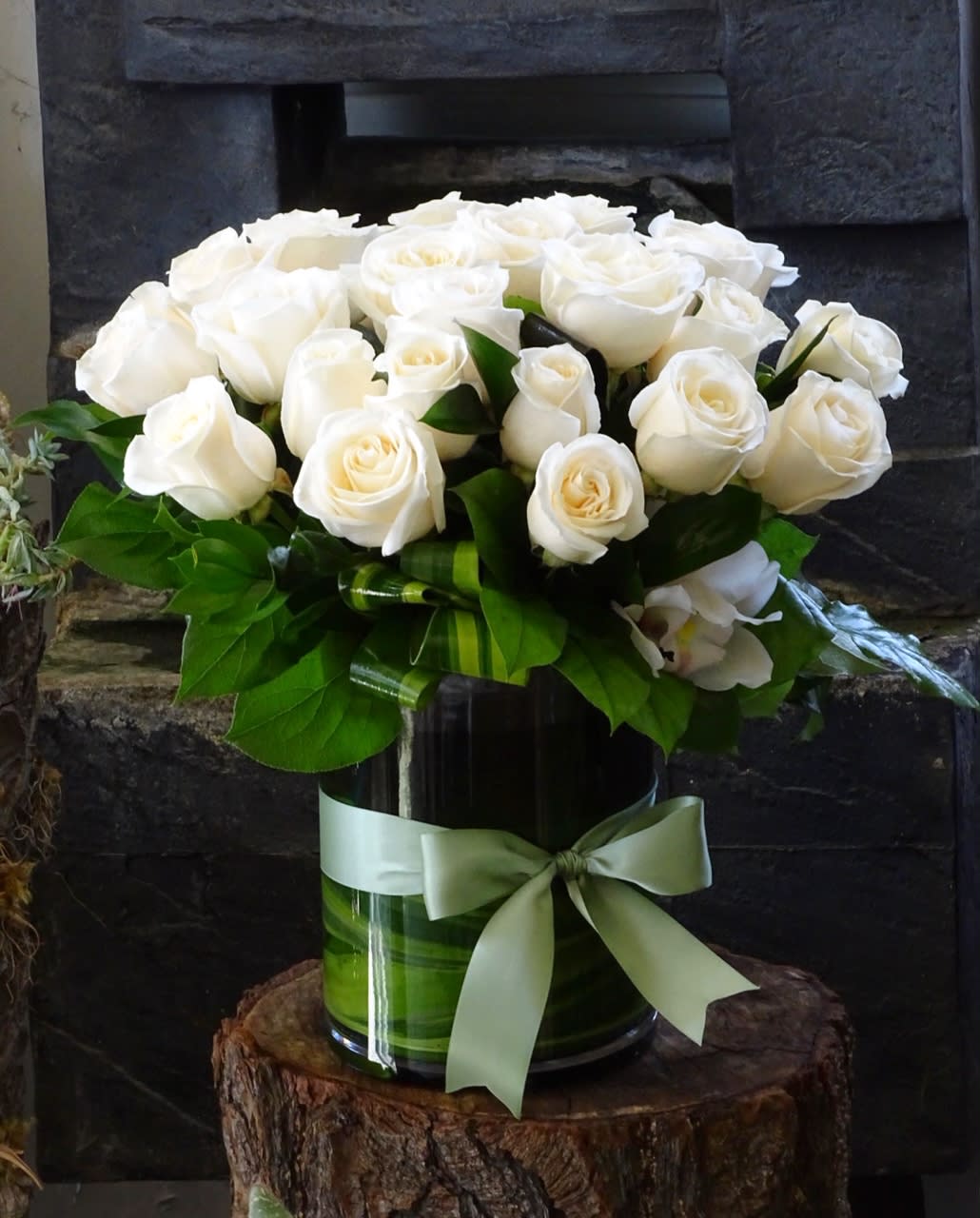 White roses arranged in a glass vase with a pale green ribbon