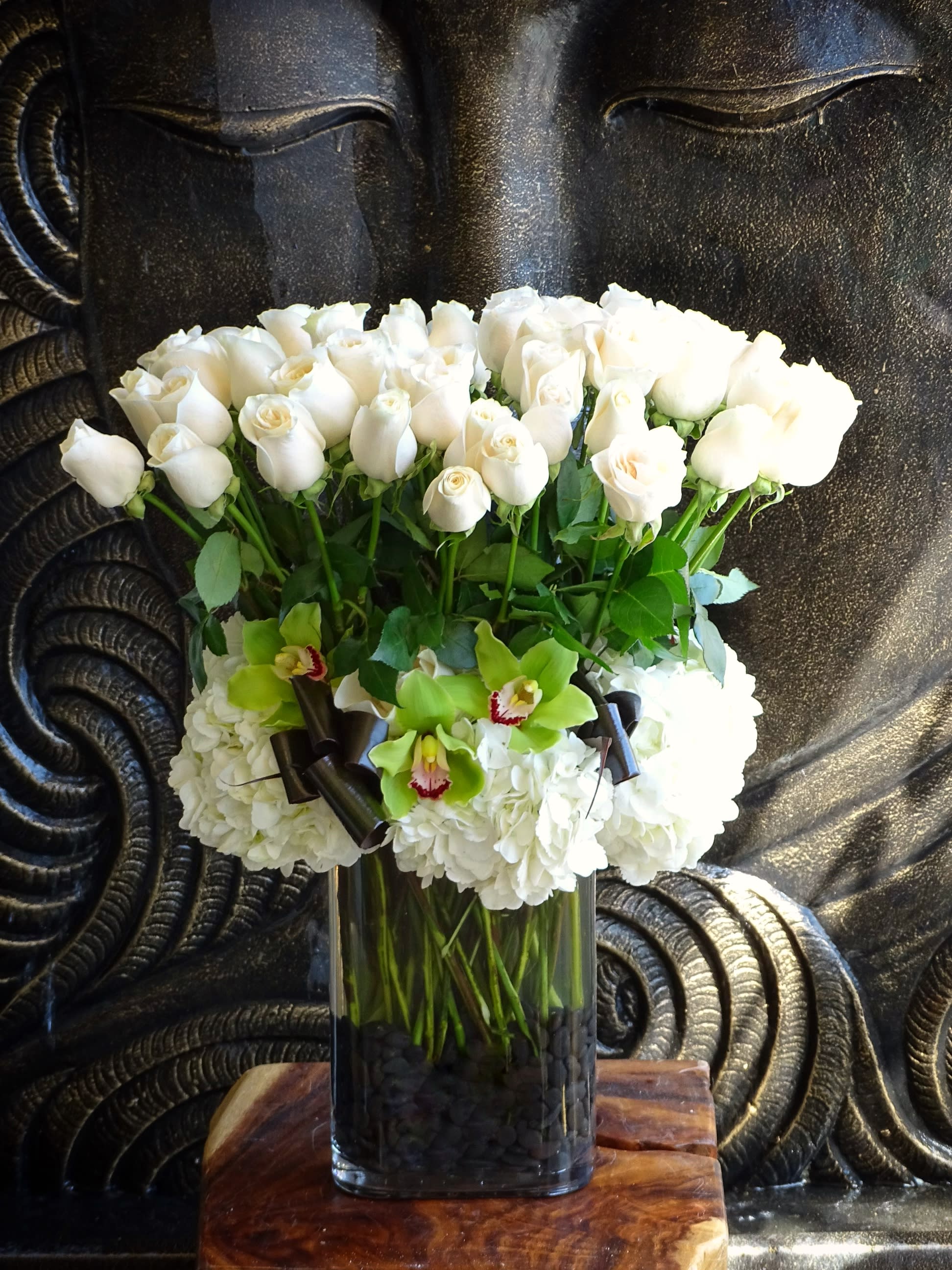 White roses and green orchids in a tall glass vase