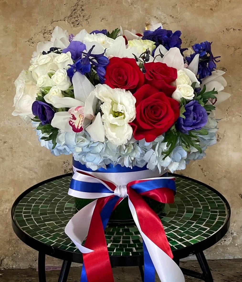 Red, white, and blue floral arrangement in a round box with ribbon
