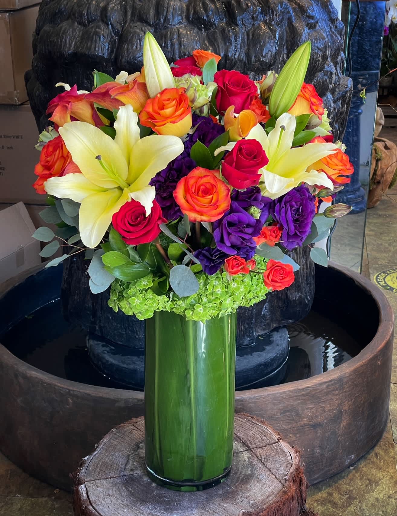 Bouquet of lilies, roses, and purple blooms in a tall green vase