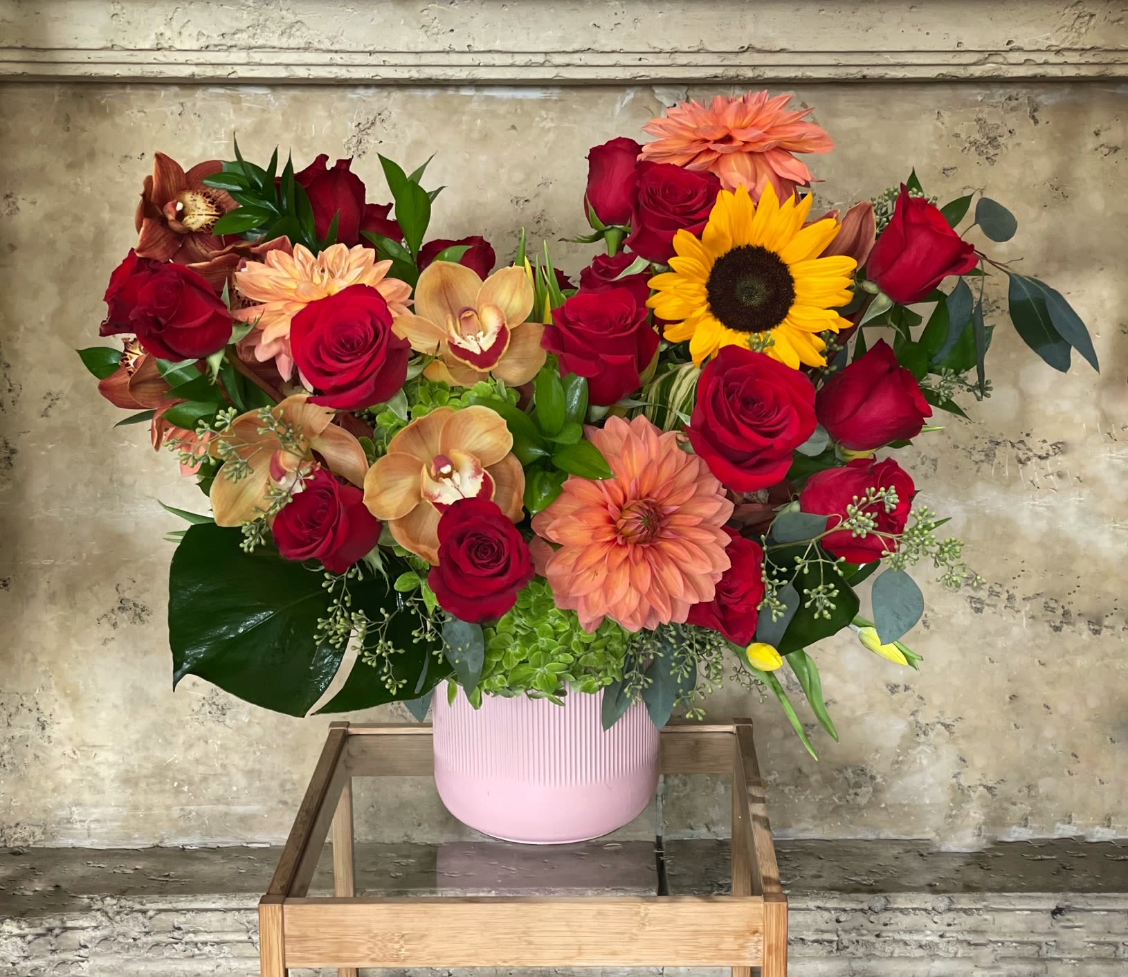 Mixed bouquet with red roses, peach dahlias, and a sunflower in a pink vase