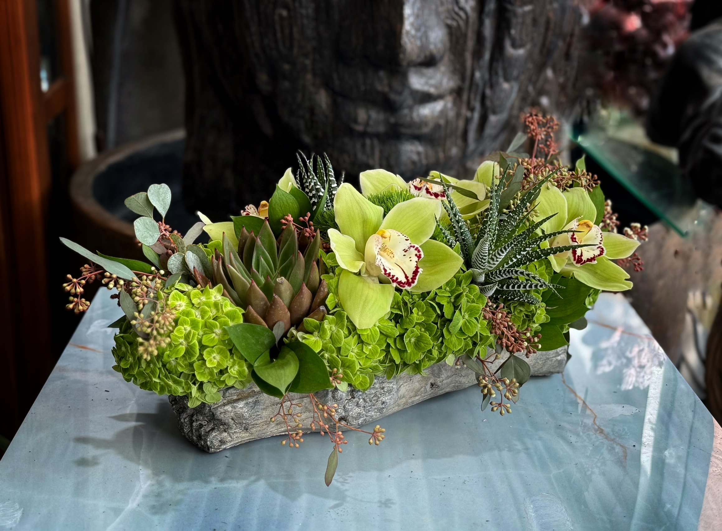 Green orchid and succulent arrangement in a rustic rectangular container