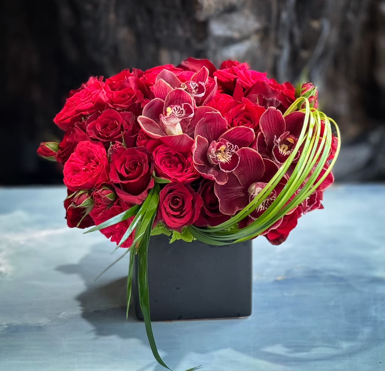 Red rose and orchid arrangement in a black square vase