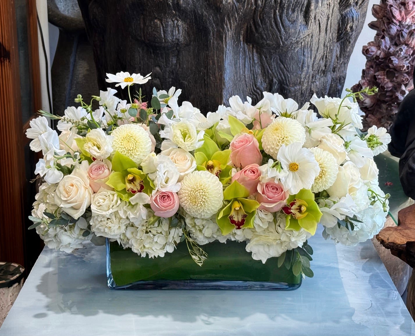 Low floral arrangement of white blooms, pink roses, and green orchids in a glass vase