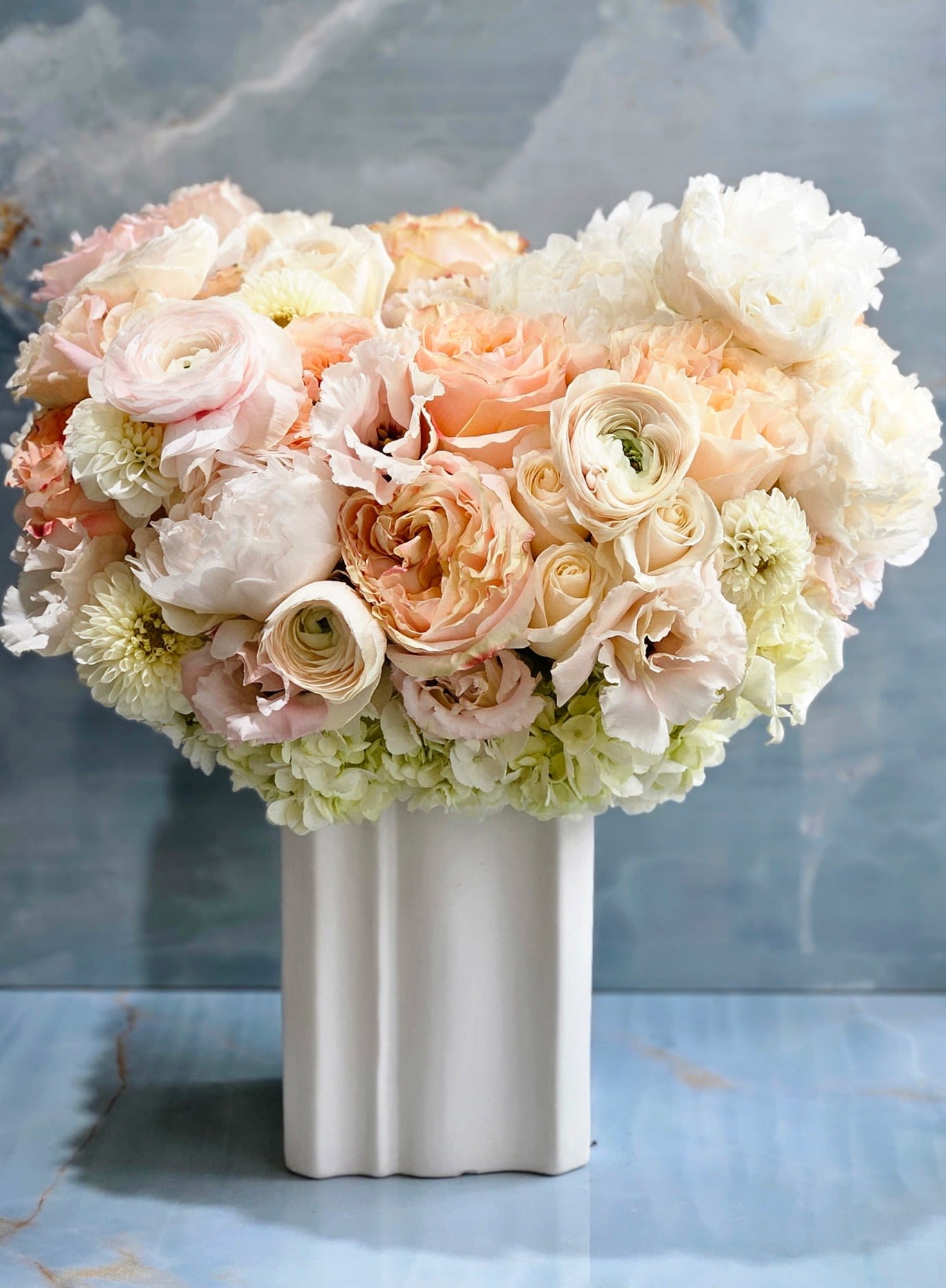 Pastel peach and white roses and ranunculus arranged in a white ceramic vase