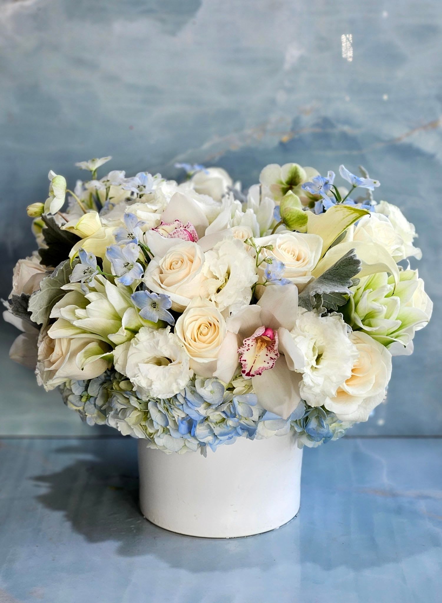 White and pale blue floral arrangement in a white vase