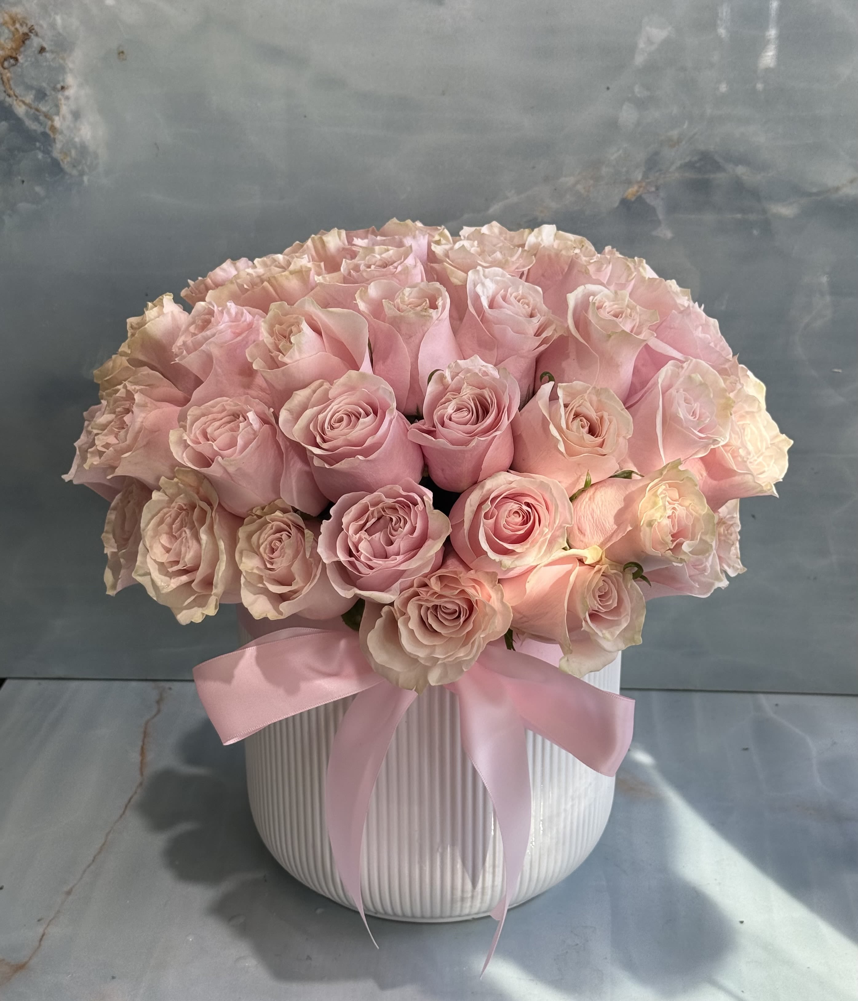 Pink roses arranged in a white ribbed vase with a pink ribbon