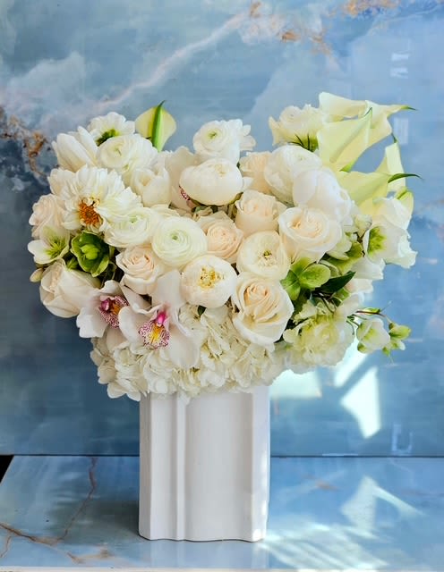 White floral arrangement in a tall white vase with calla lilies and roses