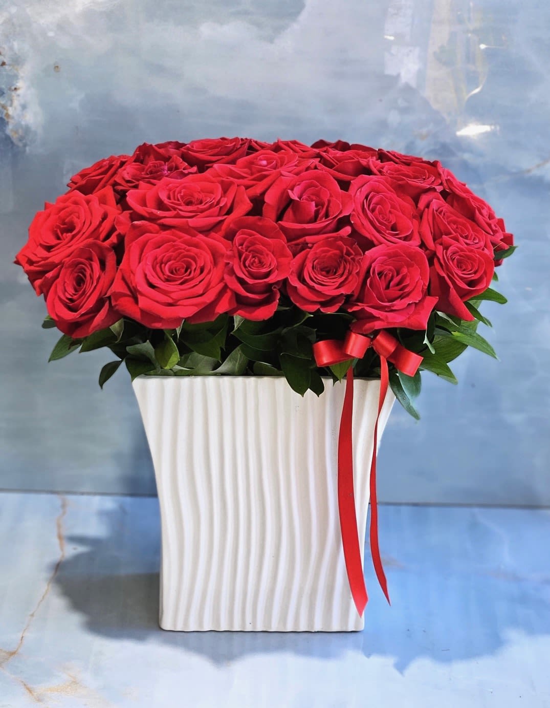 Red roses arranged in a white square vase with a red ribbon