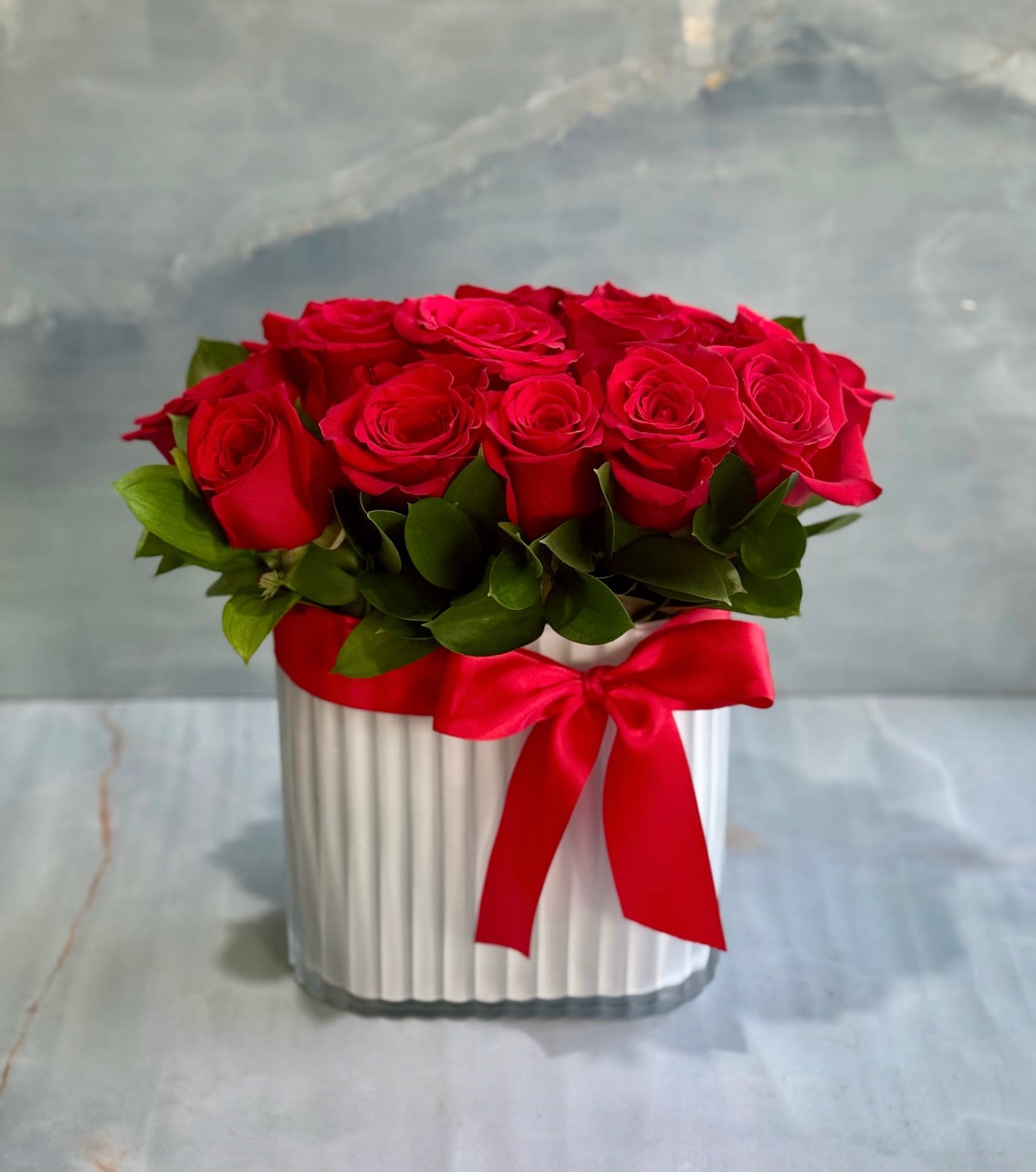 Red roses arranged in a white ribbed box with a red ribbon