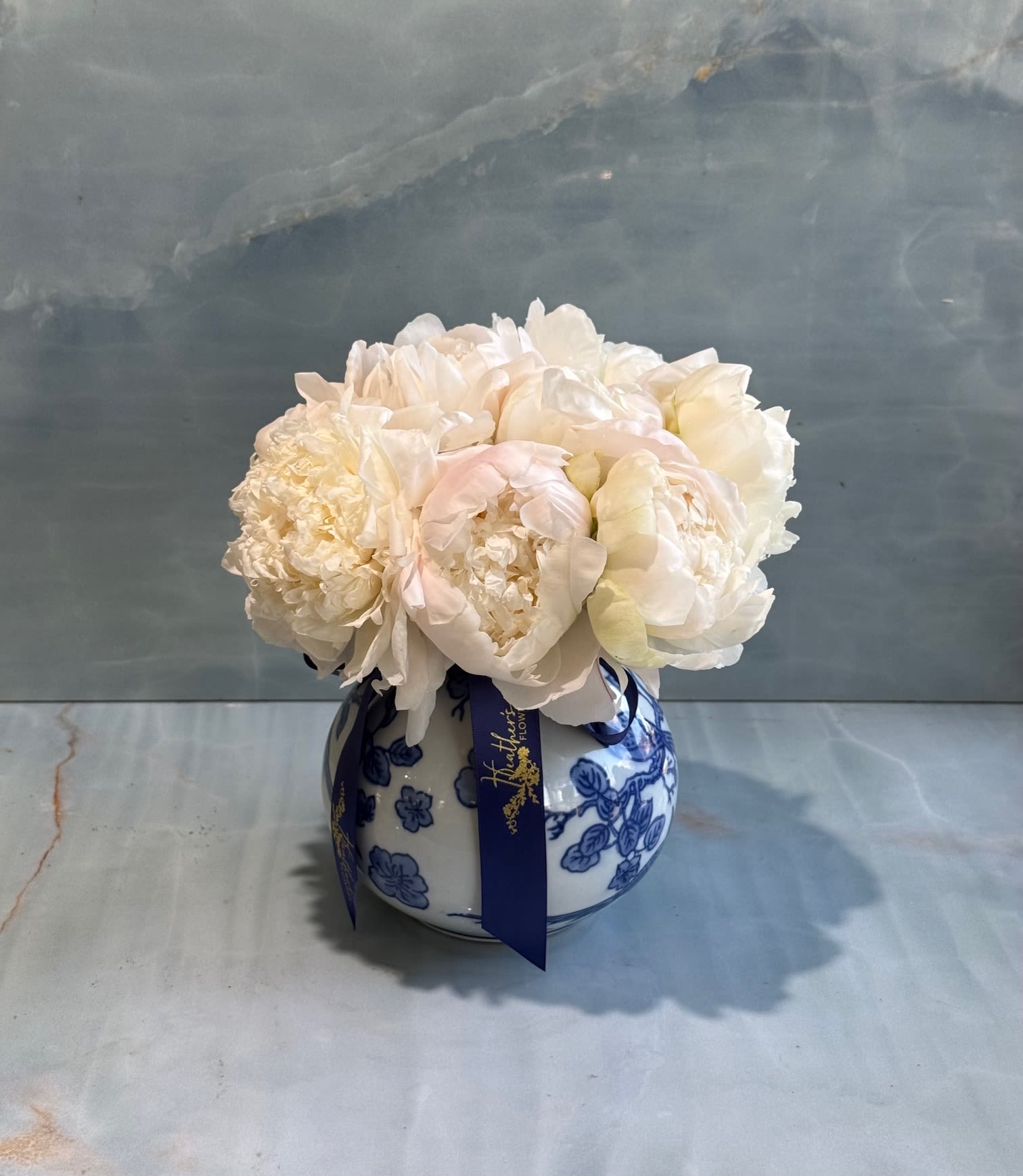 White peonies in a blue-and-white ceramic vase with a ribbon