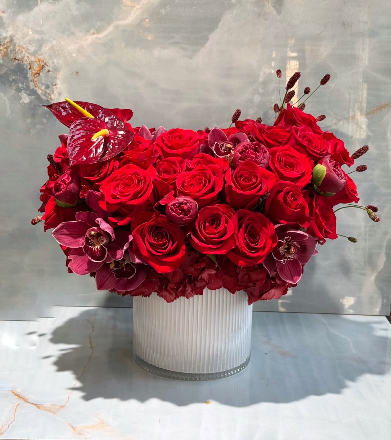 Red rose and orchid arrangement in a ribbed glass vase