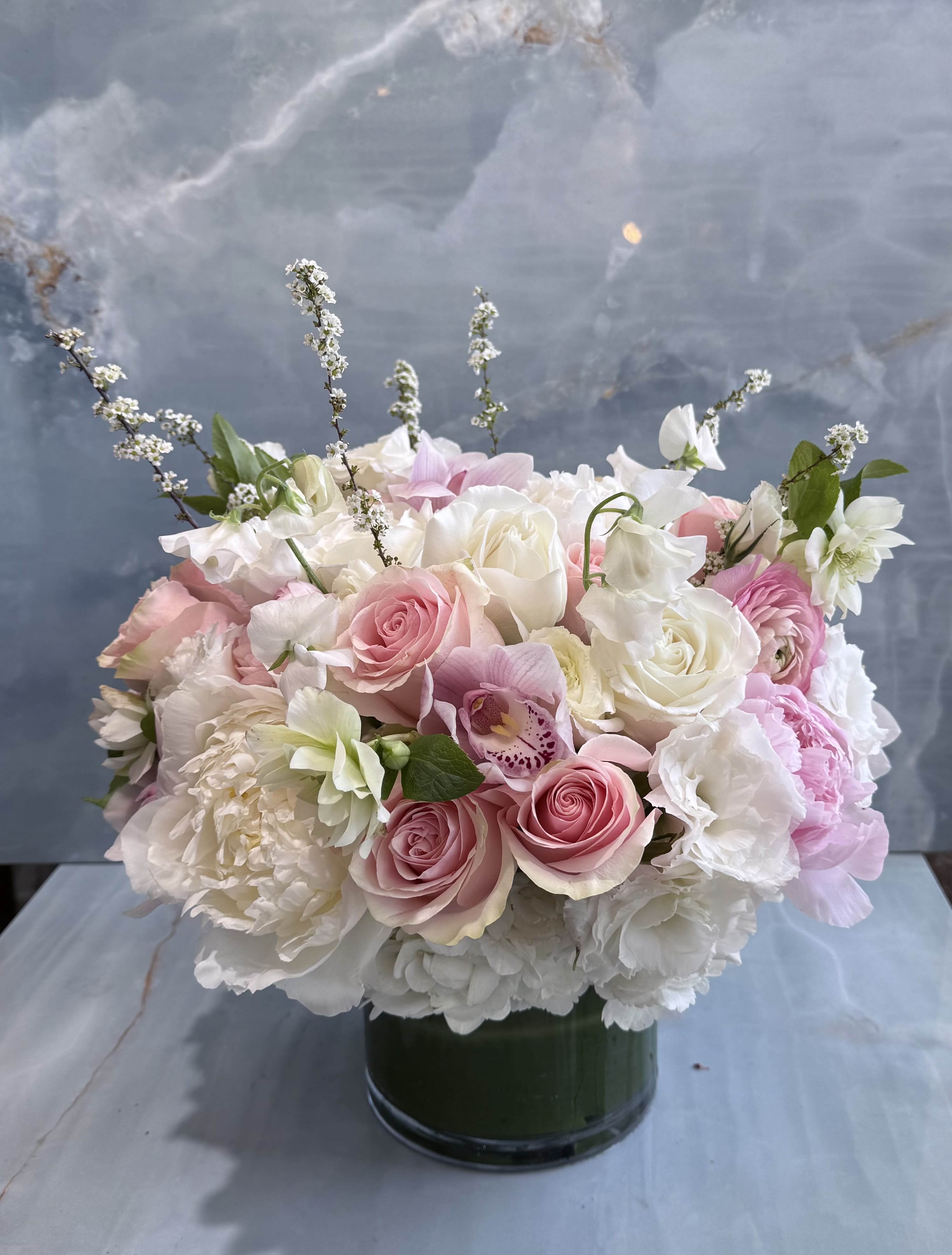 Garden Whisper - A soft, romantic blend of blush pinks and creamy whites, this arrangement feels like a fresh garden in full bloom---elegant, airy, and effortlessly timeless. Designed in a low, modern vessel, each bloom is thoughtfully layered to create a full, cloud-like silhouette with soft movement and texture. The result is a sophisticated garden-inspired piece that feels both serene and indulgent--perfect for moments that call for understated luxury. 