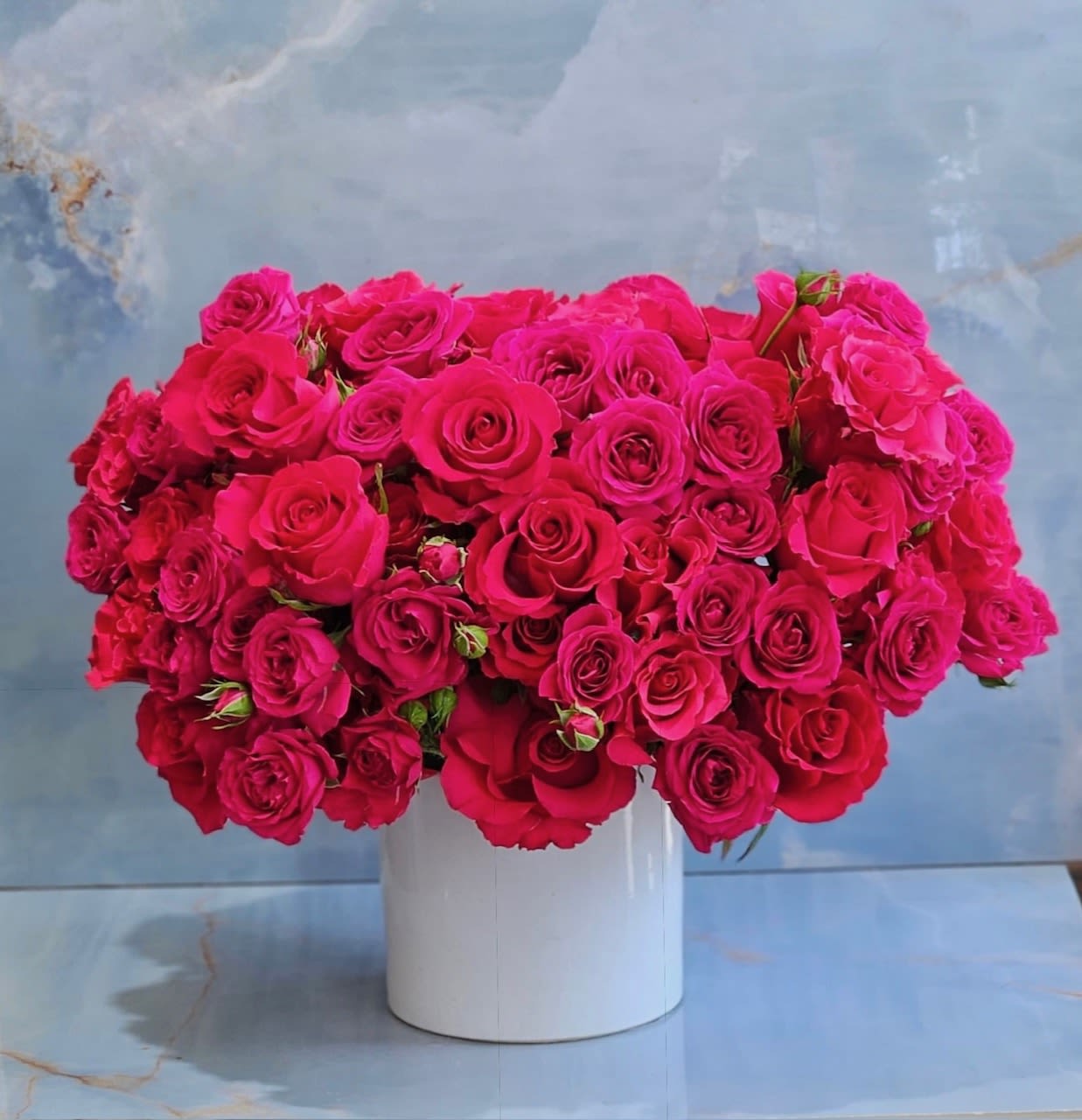 Exotic Hot Pink - This arrangement is a vibrant expression of romance and modern luxury. An abundant collection of premium hot pink roses and spray roses is artfully designed in a sleek white ceramic vessel, creating a lush, cloud-like silhouette overflowing with color. Bold yet refined, this arrangement is a stunning statement piece that transforms any space with elegance and energy. 