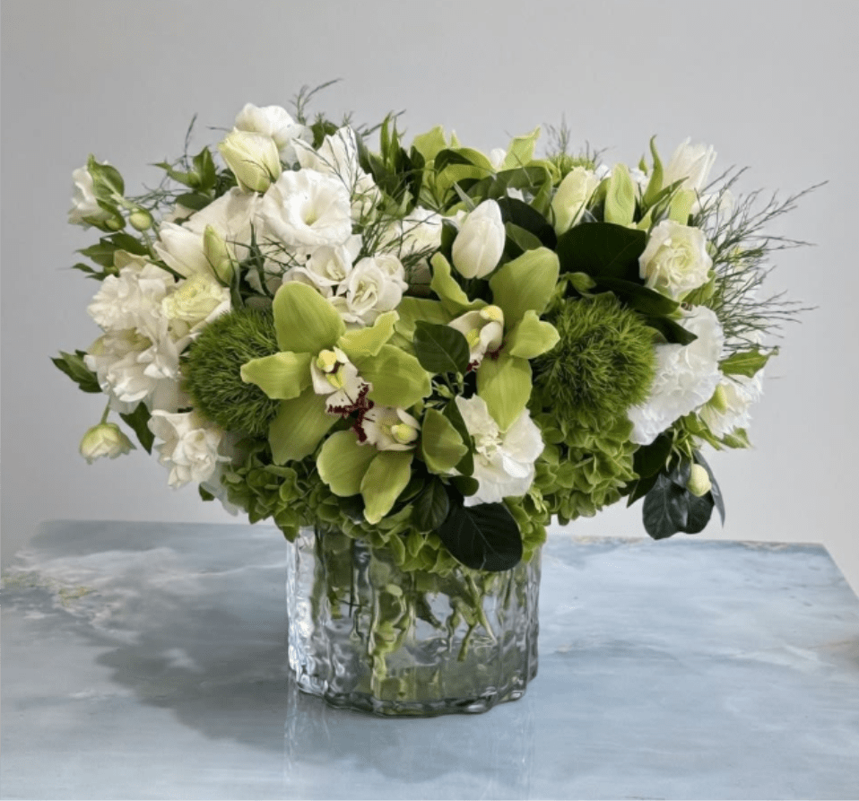 Low arrangement of white blooms and green orchids in a clear glass vase