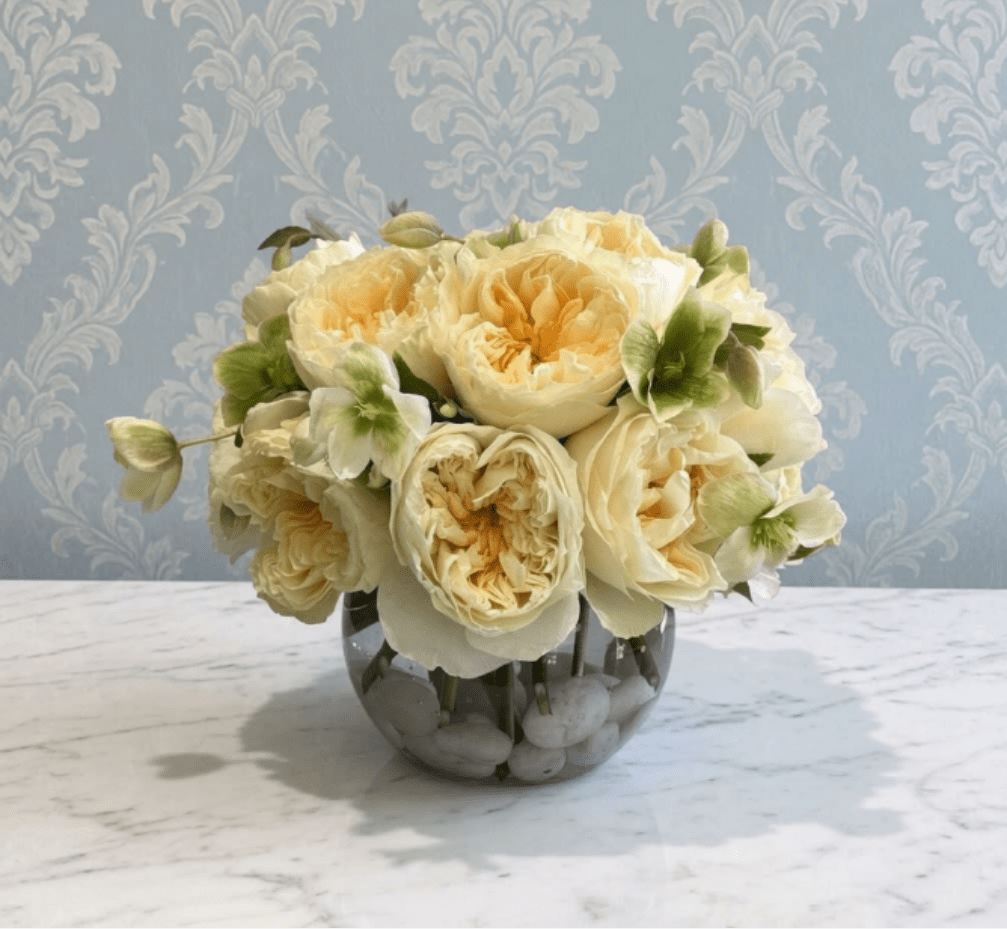RoseBowl - This arrangement is the definition of understated luxury. Featuring creamy ivory garden roses with soft butter-yellow centers, accented by delicate green hellebores, it has a timeless, romantic elegance. Arranged in a clear glass bowl with polished white stones, it feels fresh, refined, and effortlessly sophisticated. 