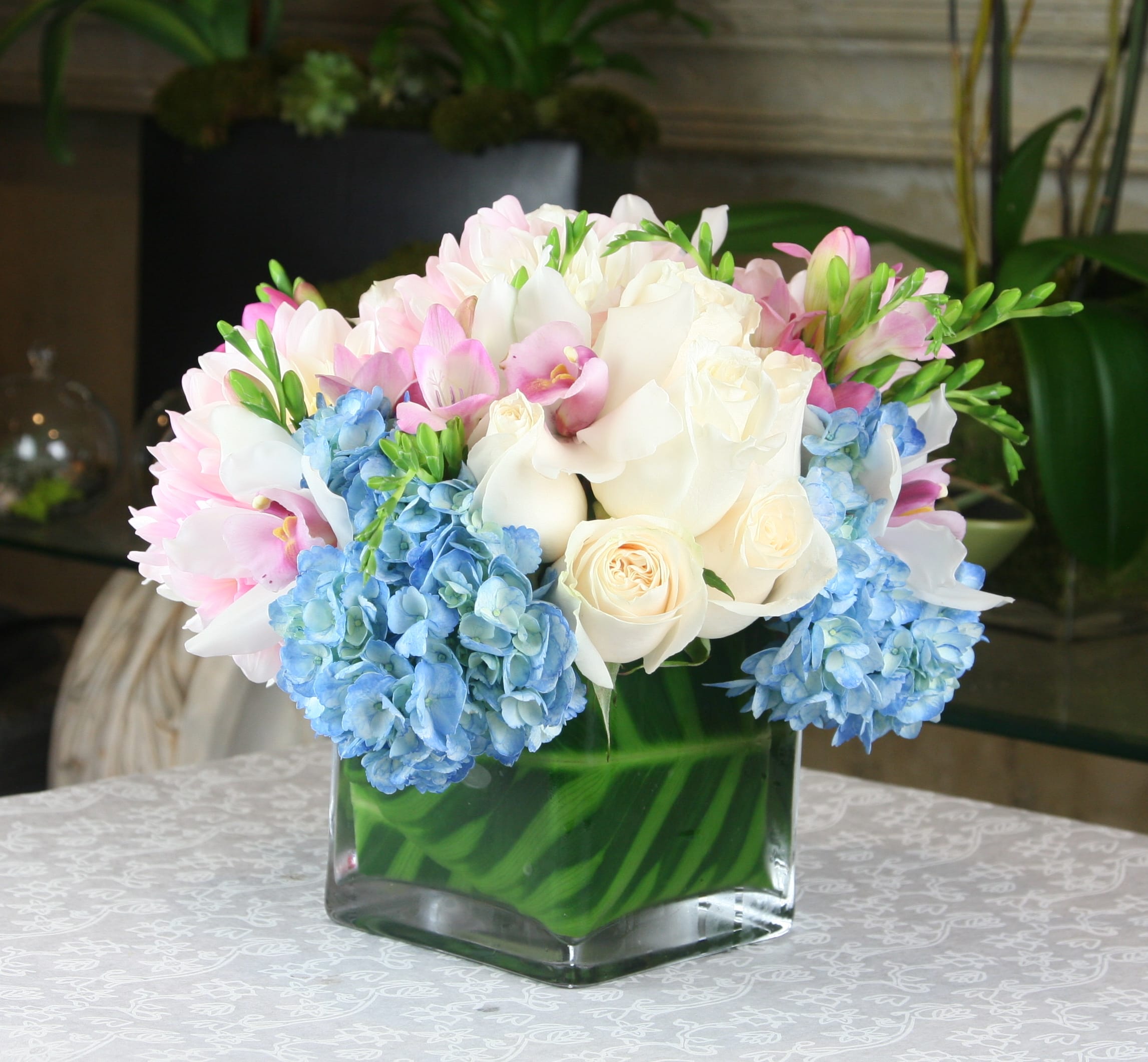 Pink and white bouquet with blue hydrangeas in a square glass vase