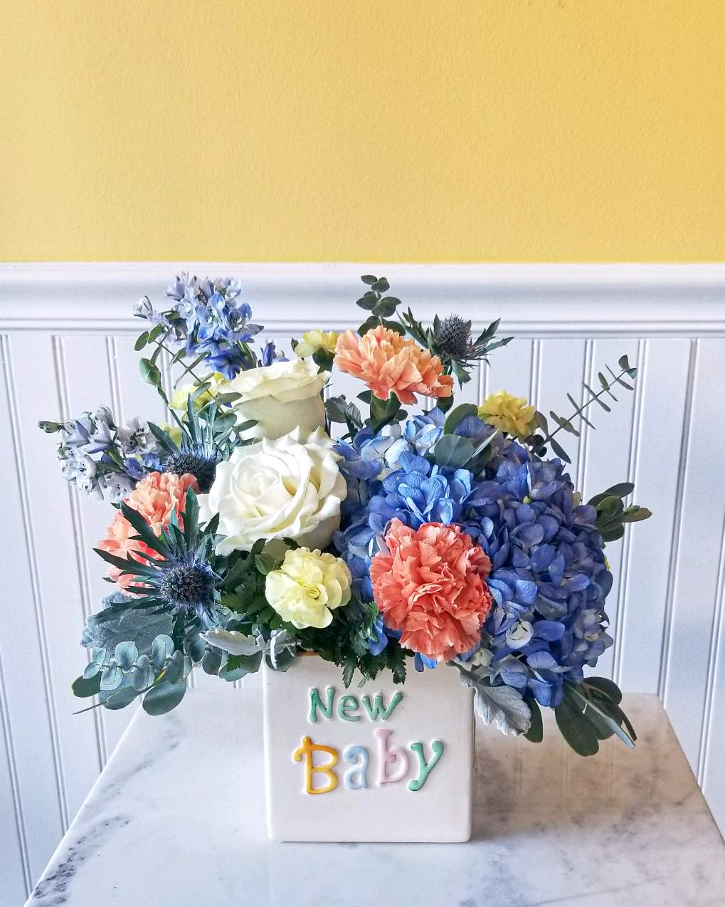 Colorful flower arrangement in a white vase labeled New Baby