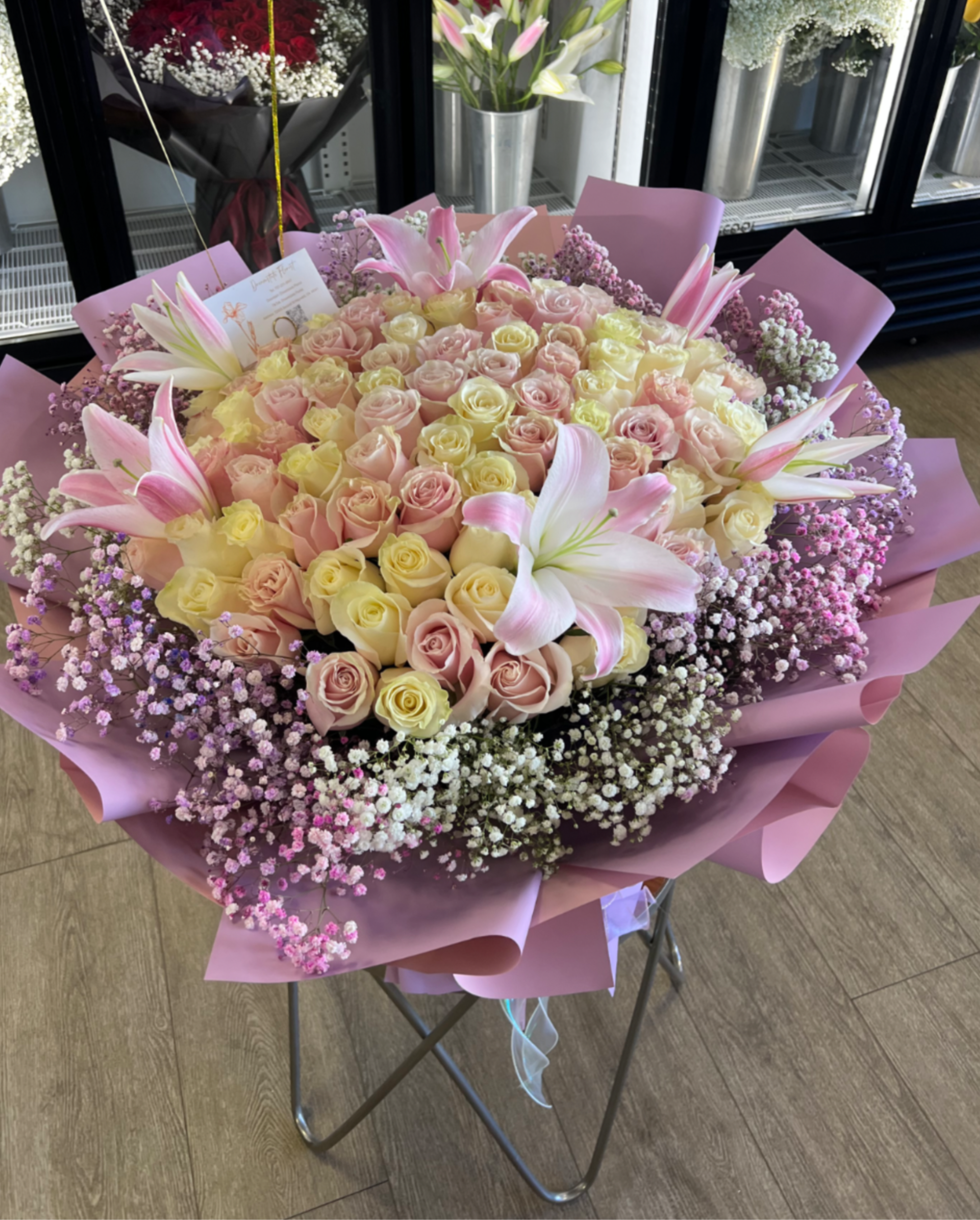 99 stems roses &amp; lilies bouquet  - Pale pink and white roses with pink-and-white lilies, framed by purple and white baby breath fillers, wrapped in layered pink paper-lush, romantic bouquet perfect for celebrations and anniversaries.