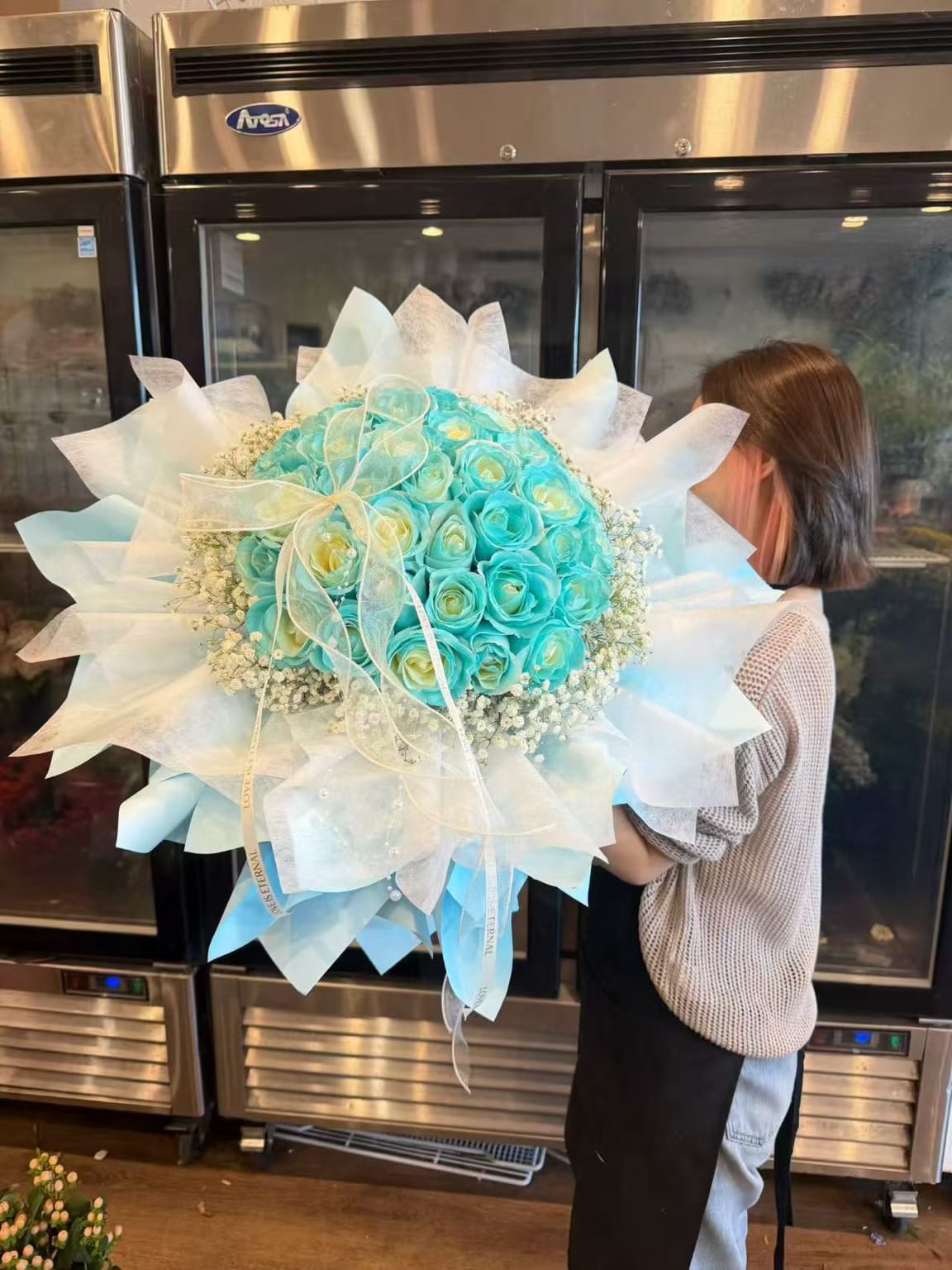 Large turquoise rose bouquet wrapped in white paper with a ribbon