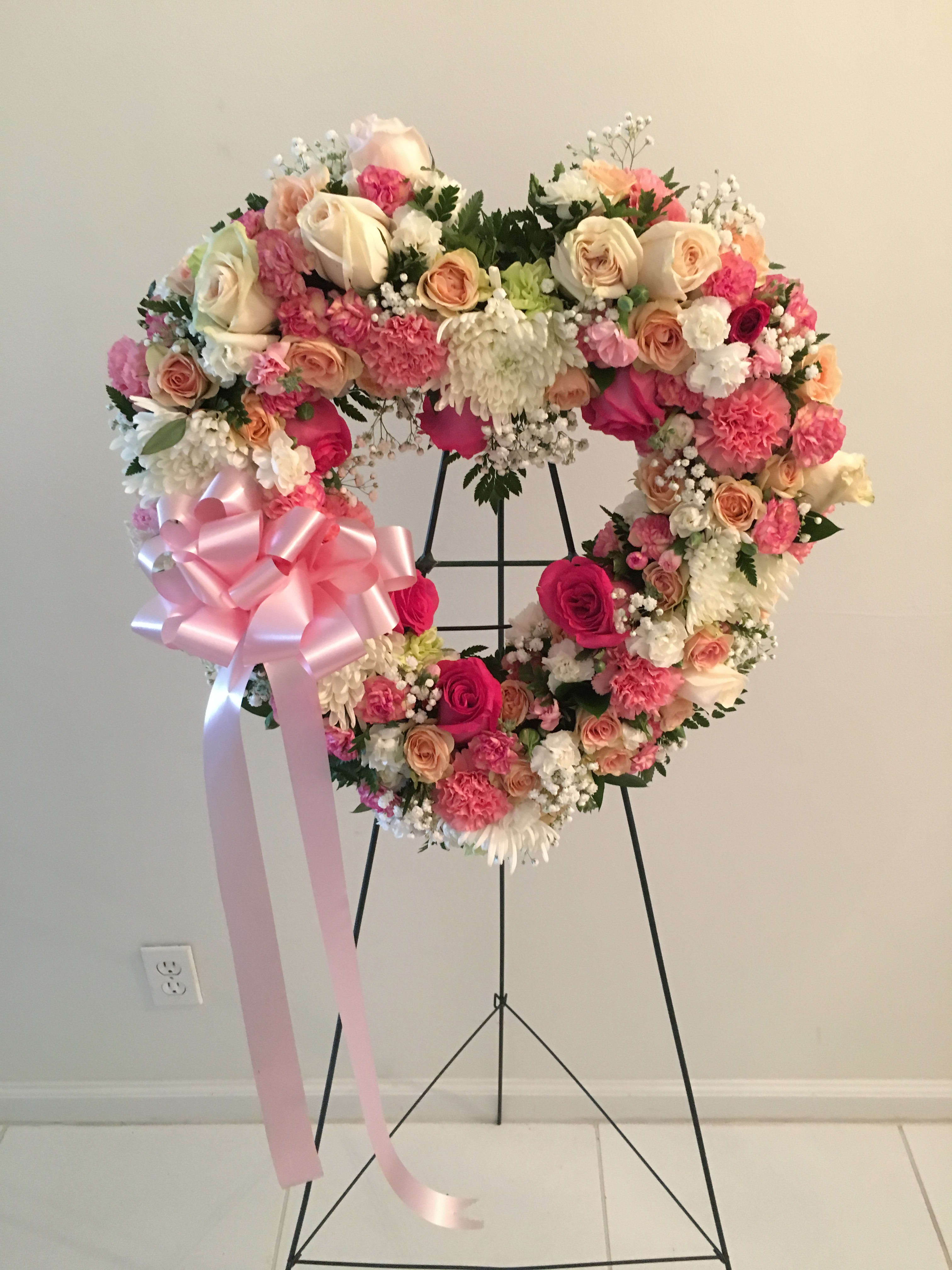 Heart-shaped floral wreath with pink and cream roses and a large pink ribbon