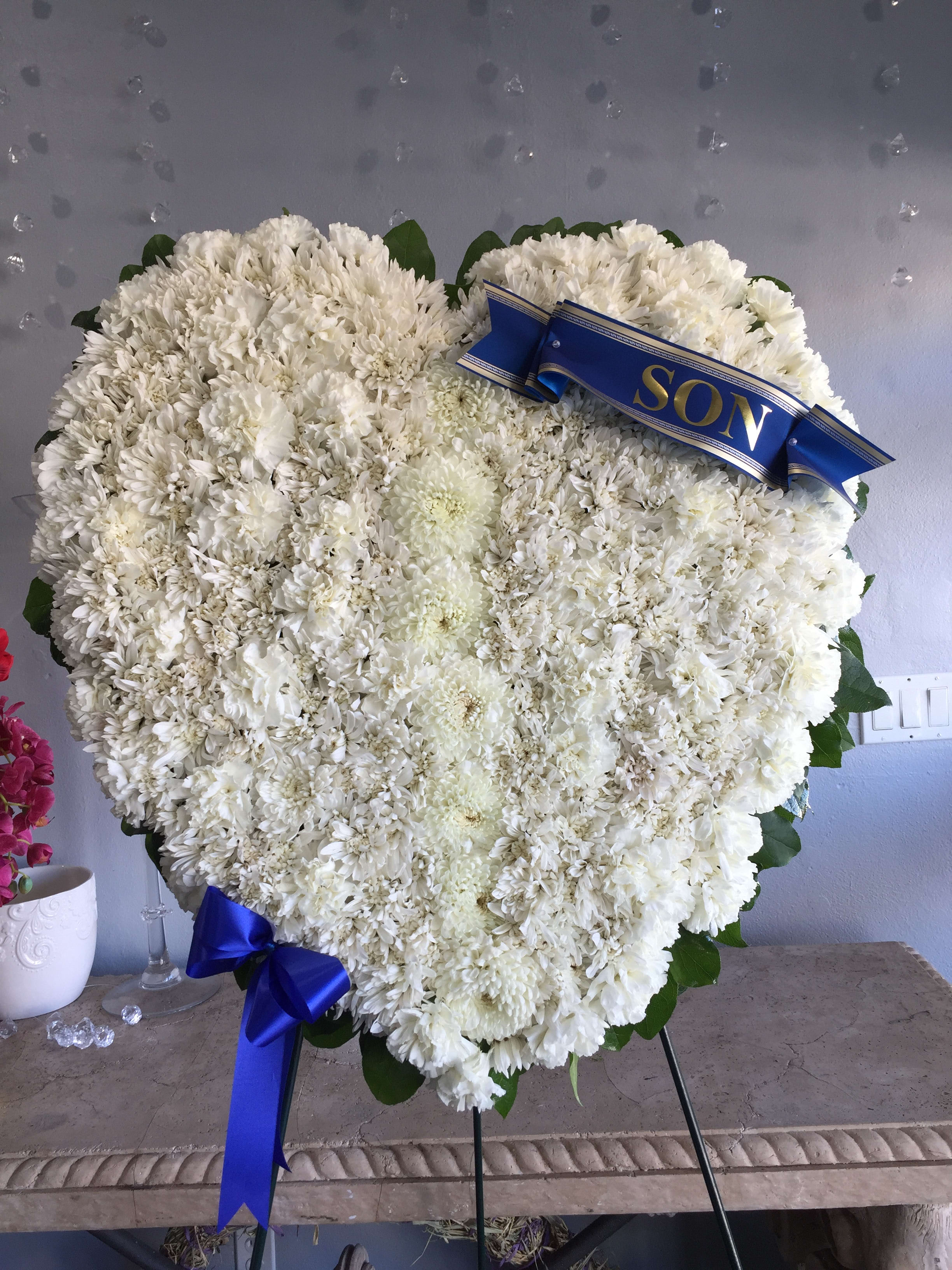 Heart-shaped white floral wreath with a blue ribbon reading SON