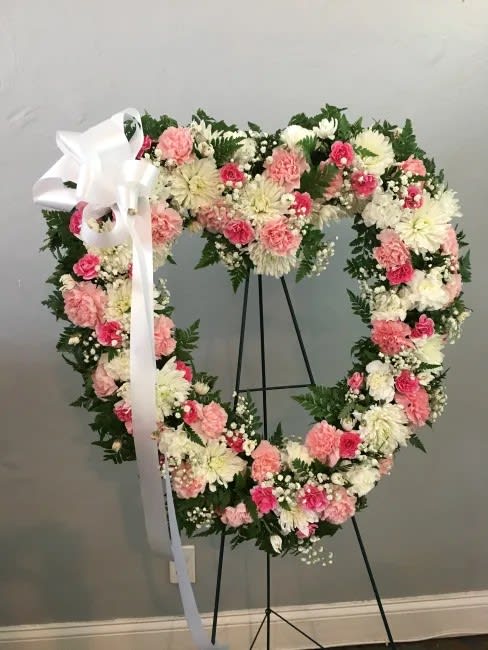 Heart-shaped floral wreath with pink and white flowers on a stand