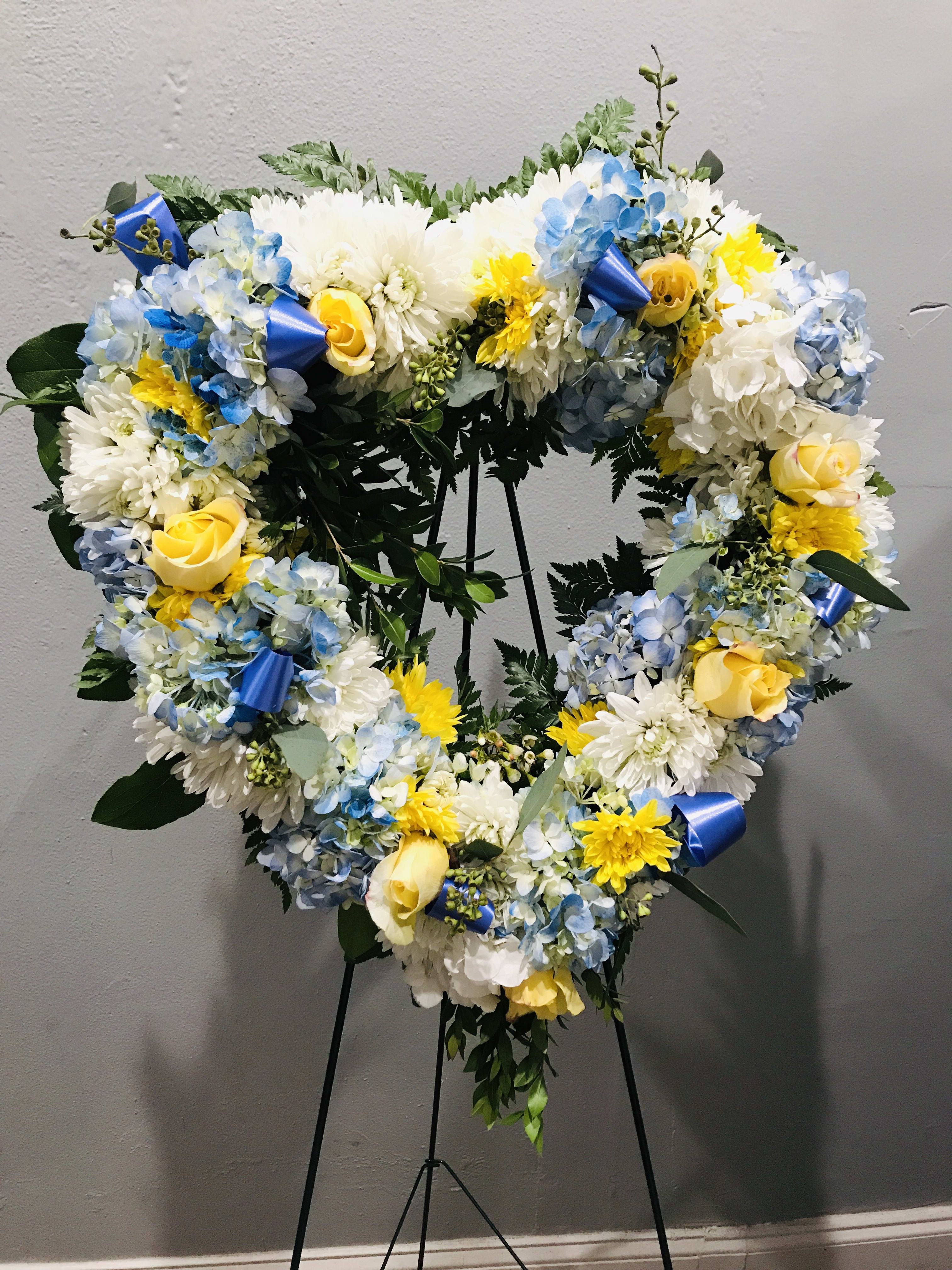 Heart-shaped floral wreath with blue, white, and yellow flowers on a stand