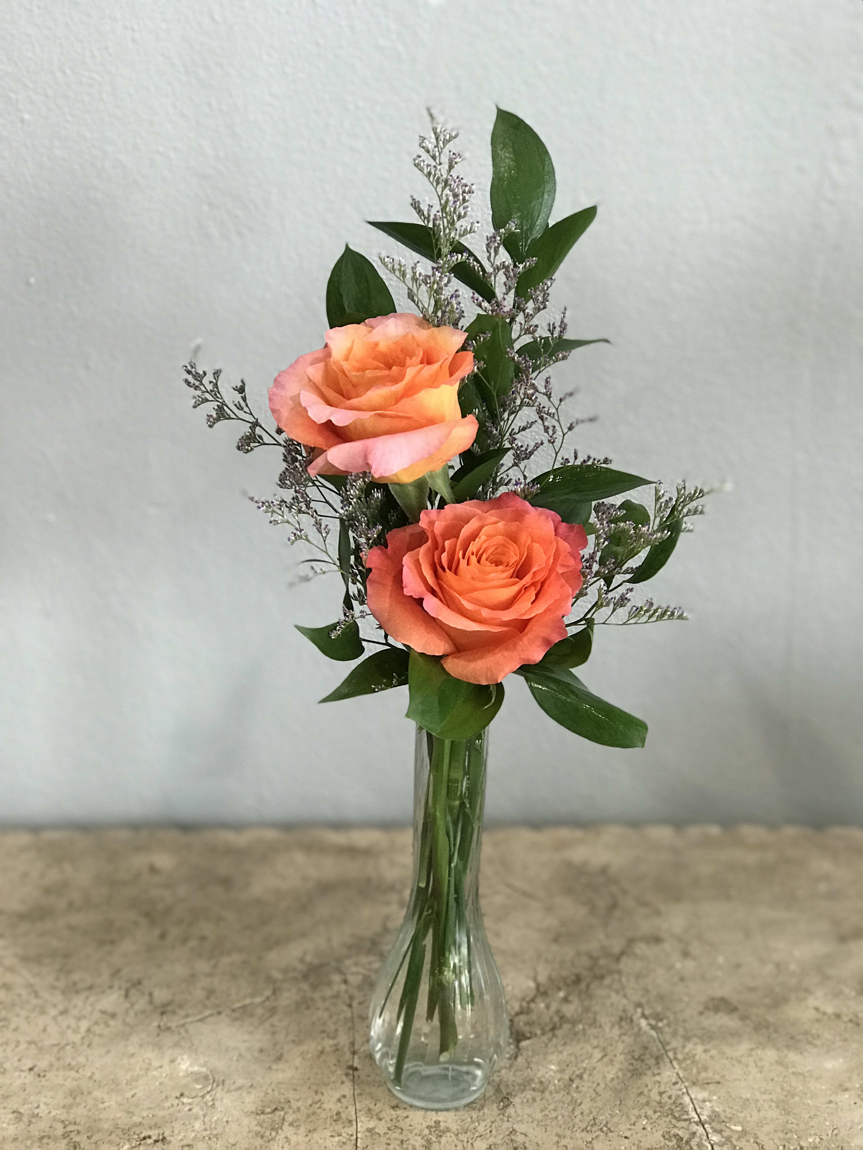 Two orange roses in a clear glass vase with greenery