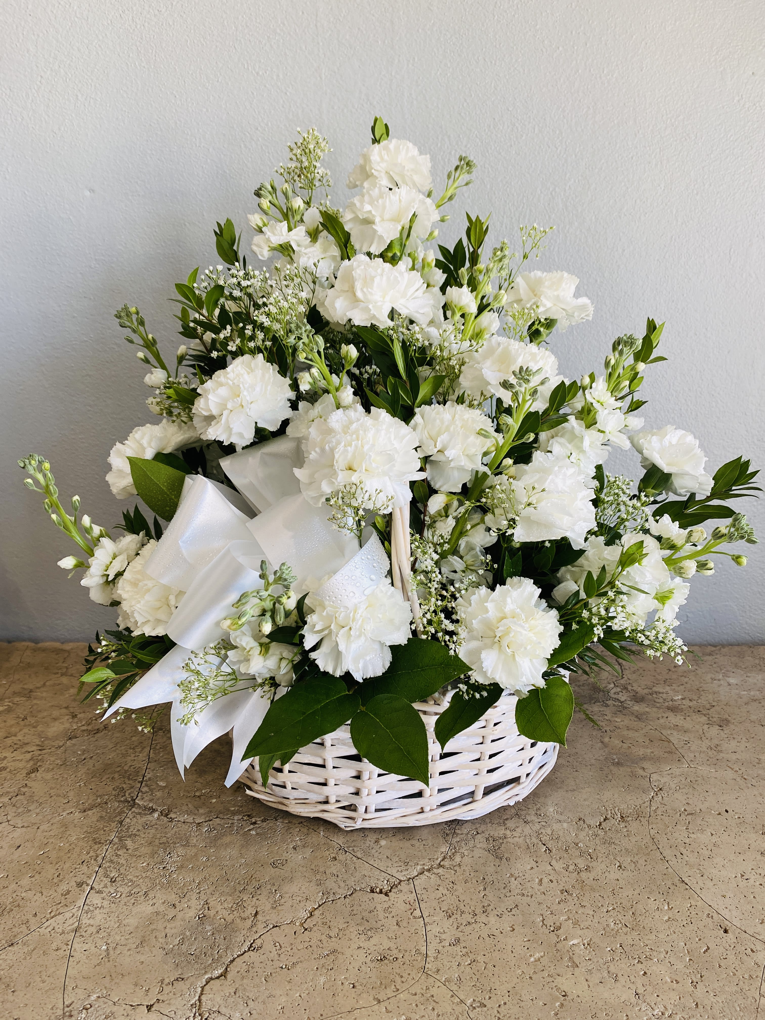 White floral arrangement in a wicker basket with a satin ribbon