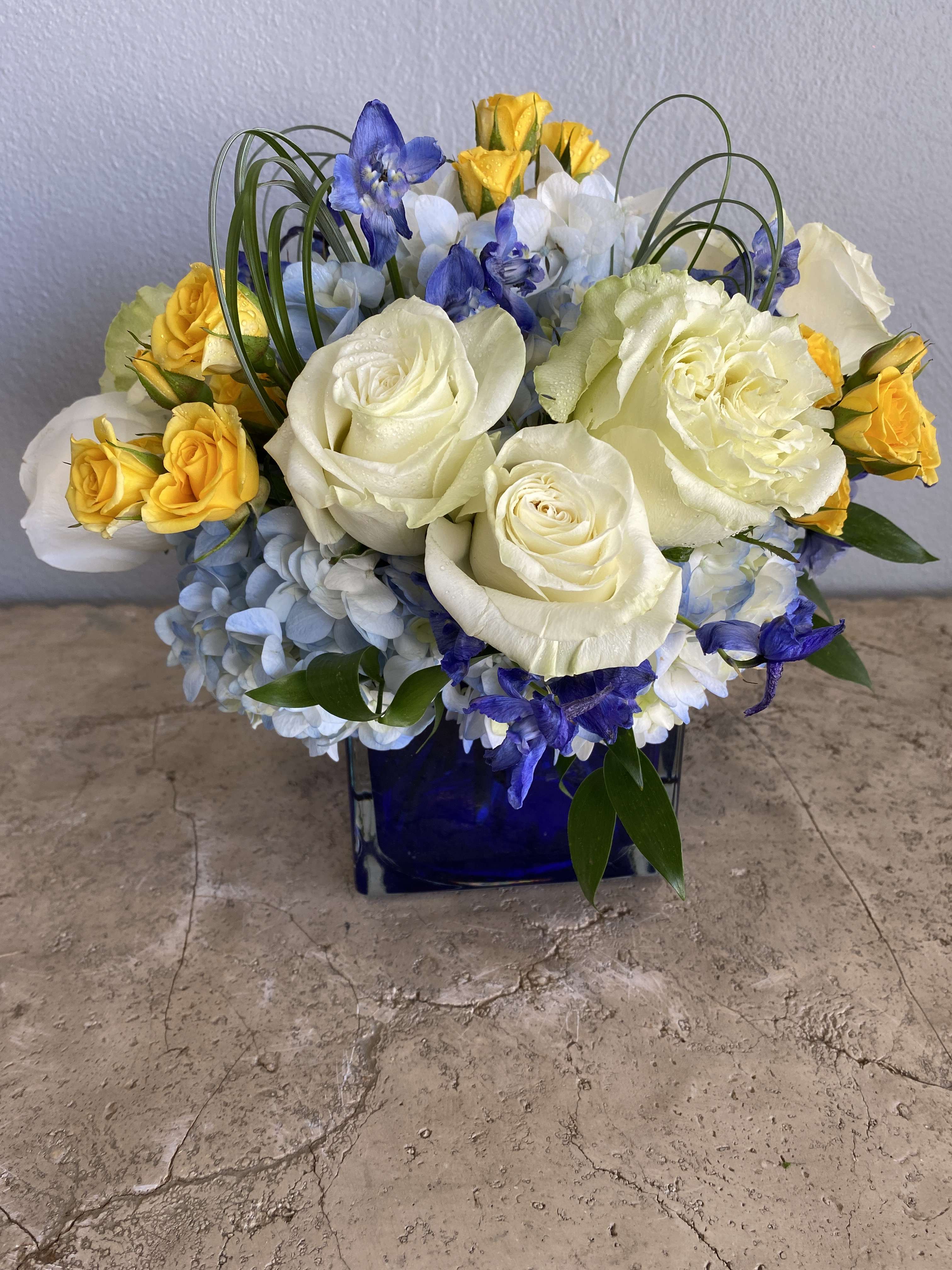 Blue and white floral arrangement with yellow roses in a cobalt vase